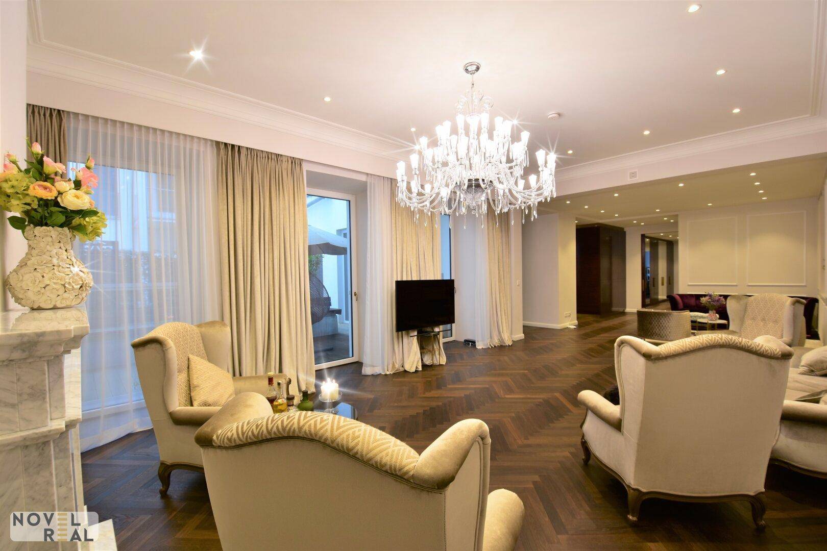 Elegantes Wohnzimmer mit Fischgrätparkett, Kronleuchter und Zugang zu einer Außenterrasse.