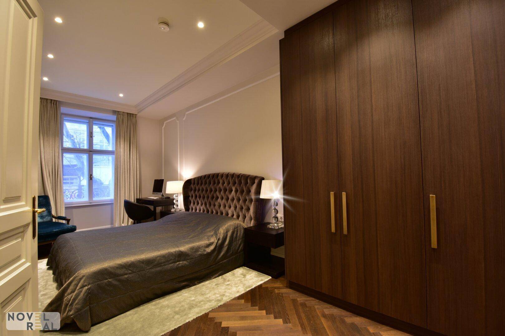 Geräumiges Schlafzimmer mit großem Polsterbett, dunklem Kleiderschrank und Fenster.