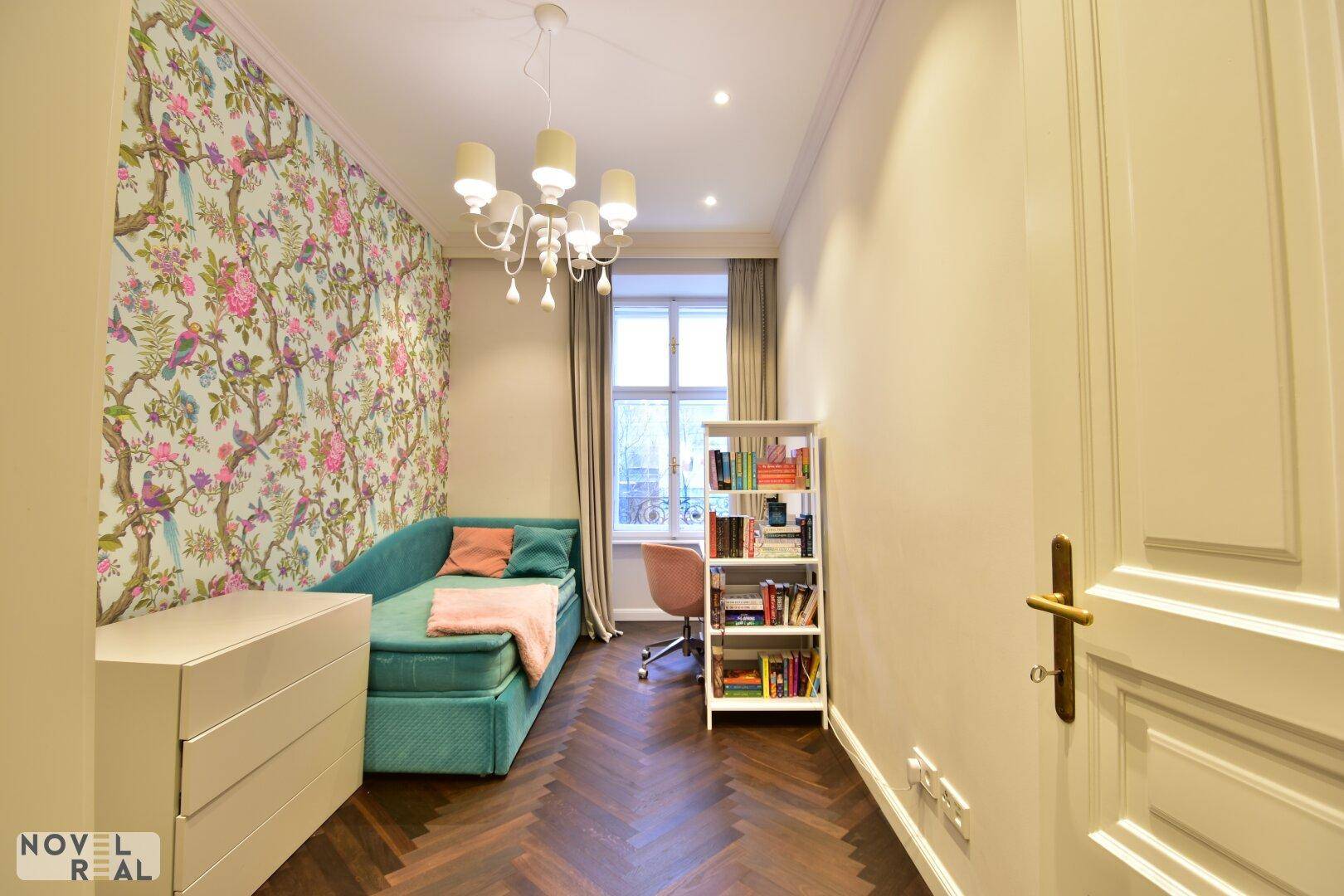 Charmantes Kinderzimmer mit floraler Tapete, Tagesbett und Bücherregal.