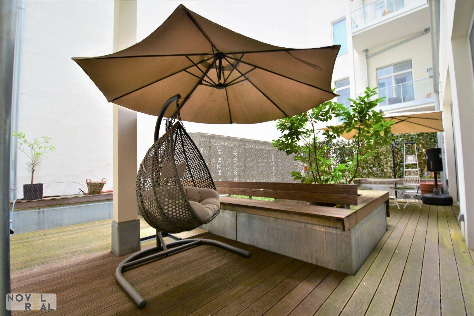 Weitläufige Terrasse mit Holzdeck, bequemer Hängeschaukel und großem Sonnenschirm.
