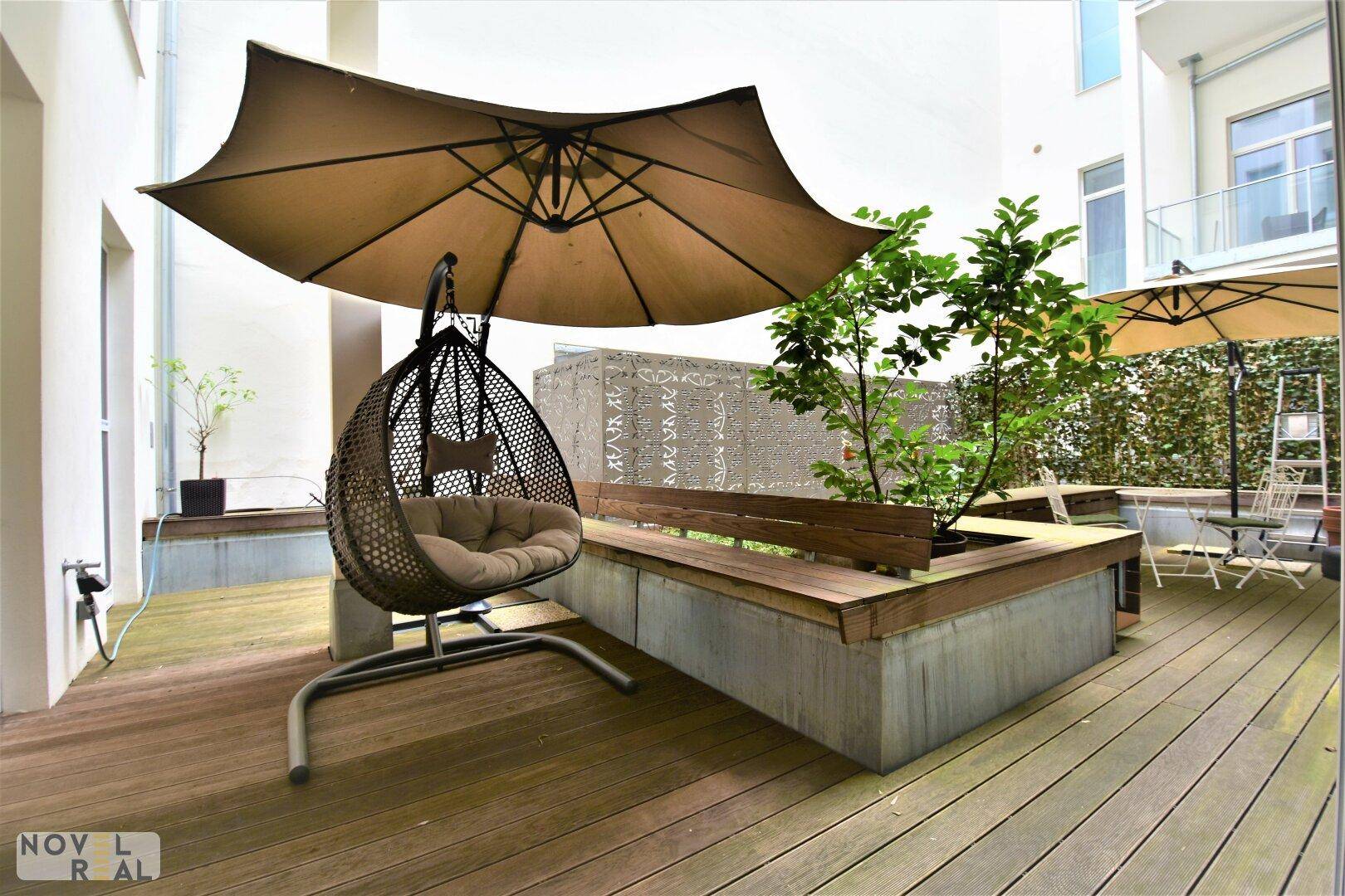 Geräumige Terrasse mit Holzdeck, bequemer Hängeschaukel und Sonnenschirm für entspannte Stunden.