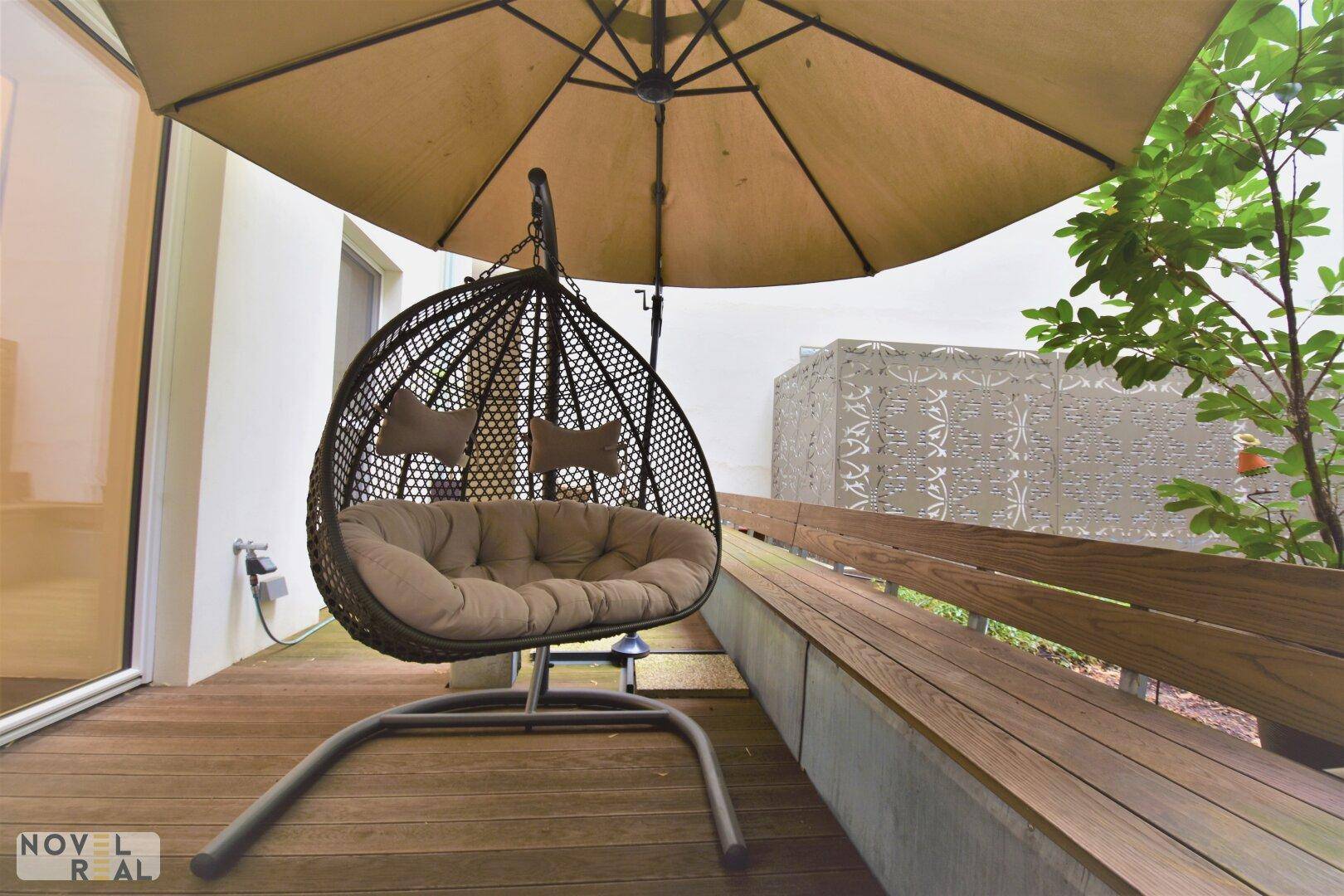 Detailansicht der Terrasse mit gemütlicher Hängeschaukel und großem Sonnenschirm auf Holzdeck.