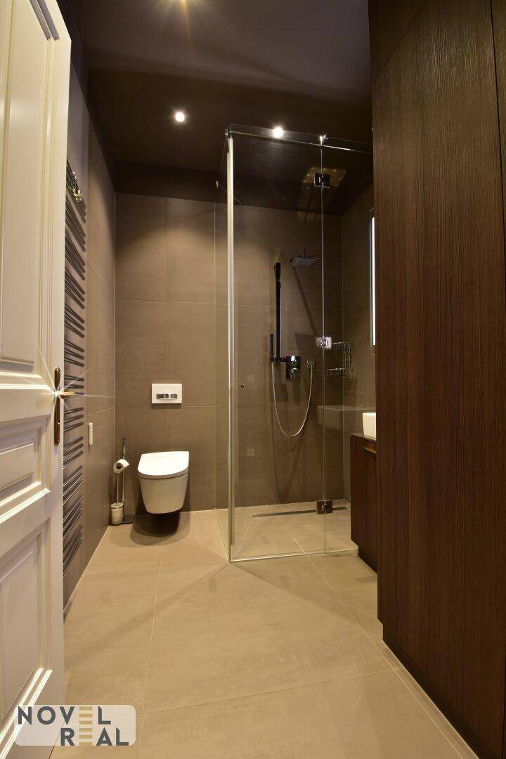 Modernes Badezimmer mit ebenerdiger Dusche, dunklen Fliesen und beheiztem Handtuchhalter.