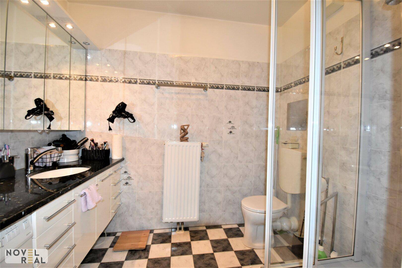 Badezimmer mit Duschkabine, Schachbrettmuster-Fliesenboden und modernem Waschtisch.