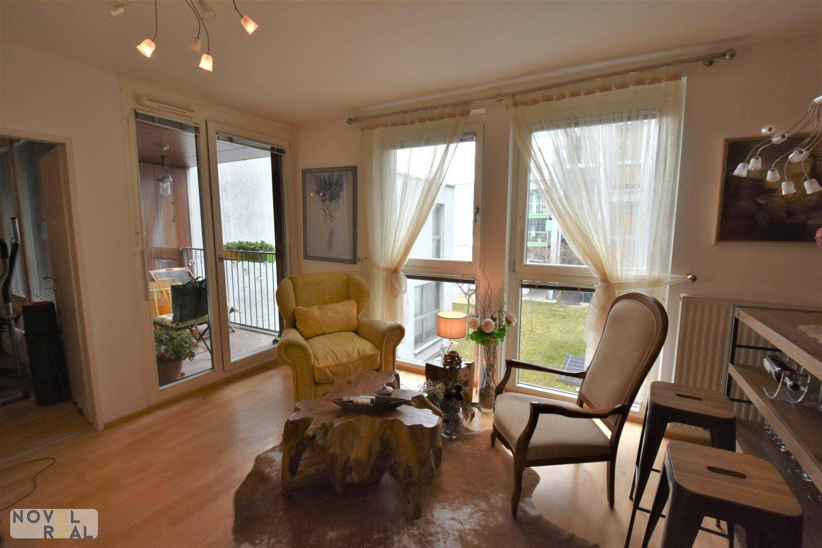 Helles Wohnzimmer mit Zugang zum Balkon, großen Fenstern und Holzboden.