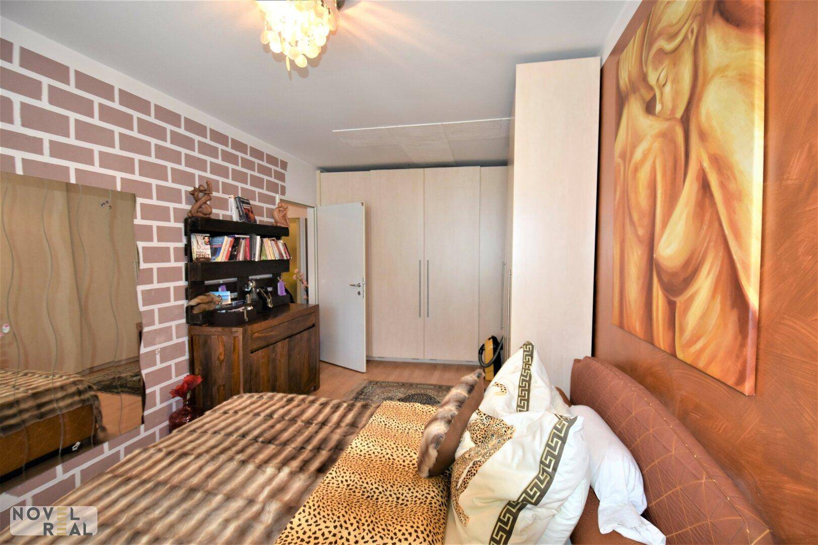 Schlafzimmer mit Holzboden, großem Spiegel und dekorativer Ziegelsteinwand.