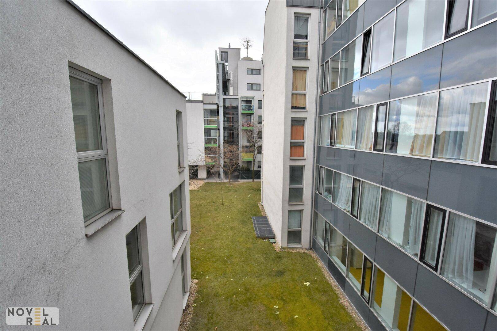 Blick auf die moderne Gebäudefassade und den begrünten Innenhof der Wohnanlage.