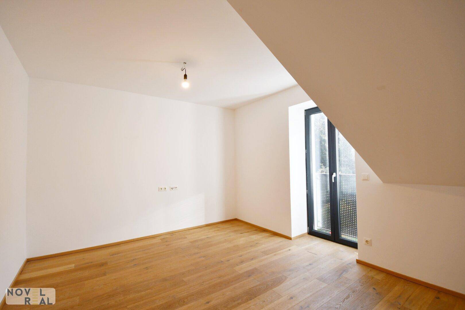 Gemütliches Schlafzimmer mit Holzboden, Dachschräge und Fenster für natürliches Licht.