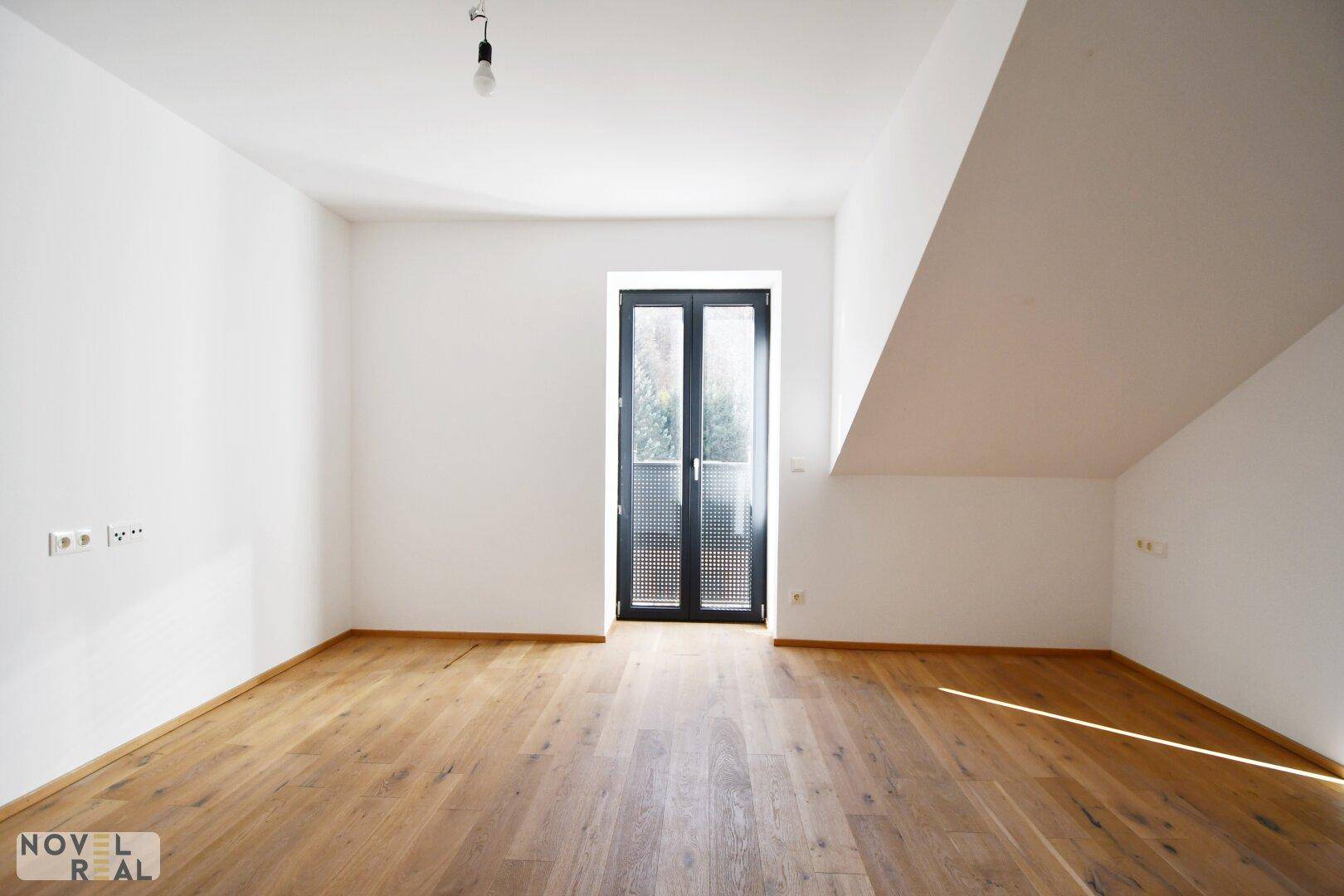 Helles Schlafzimmer mit Holzboden und Zugang zu einem französischen Balkon.