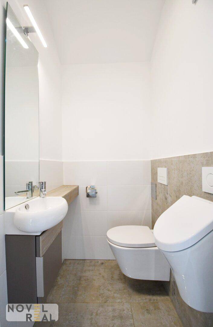Modernes Gäste-WC mit wandhängender Toilette, Urinal und kleinem Waschbecken.