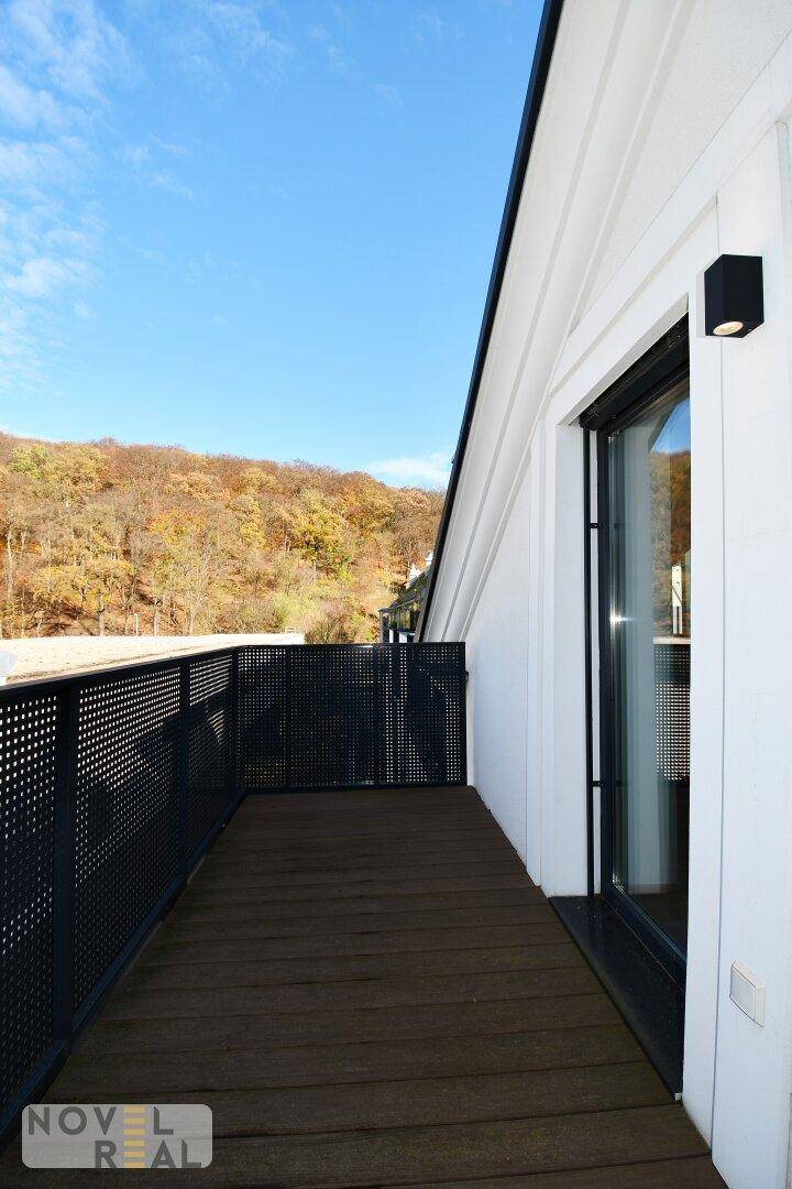 Langer Balkon mit Holzboden und schwarzem Geländer, umgeben von Natur.