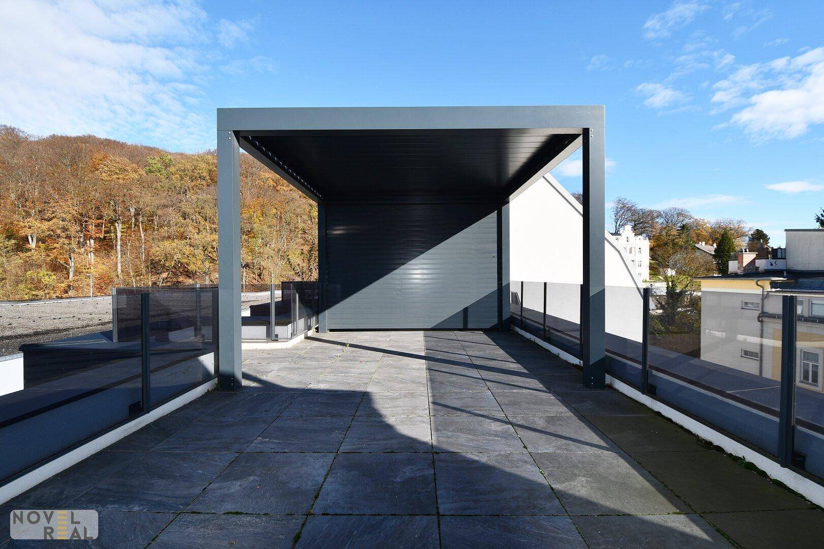 Große Dachterrasse mit moderner Pergola und Blick auf die bewaldete Umgebung.