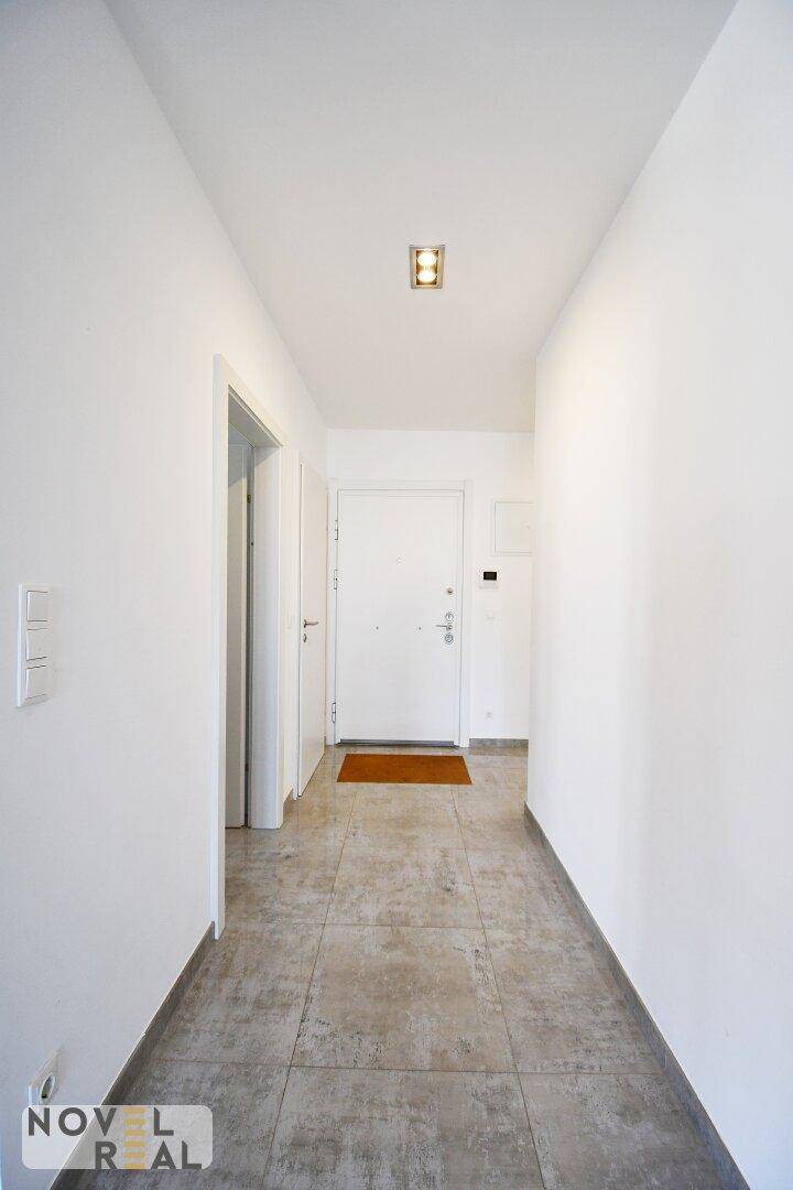 Heller Flur mit Fliesenboden und weißer Eingangstür, der zu den Zimmern führt.