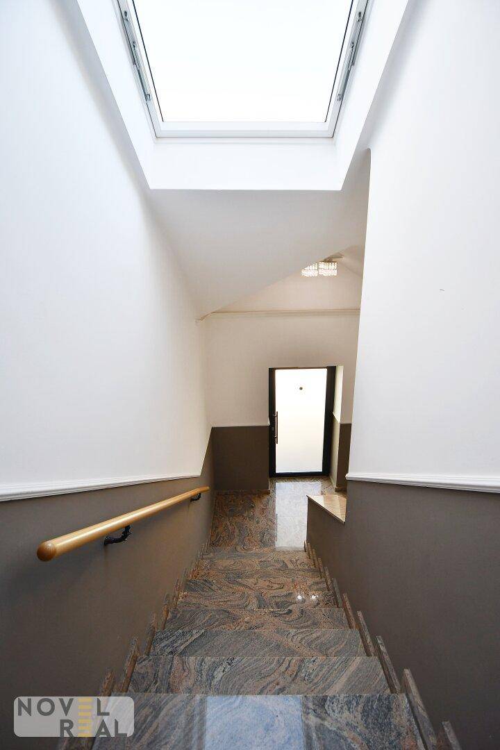 Treppenhaus mit Marmorstufen, Holzgeländer und Dachfenster für natürliches Licht.