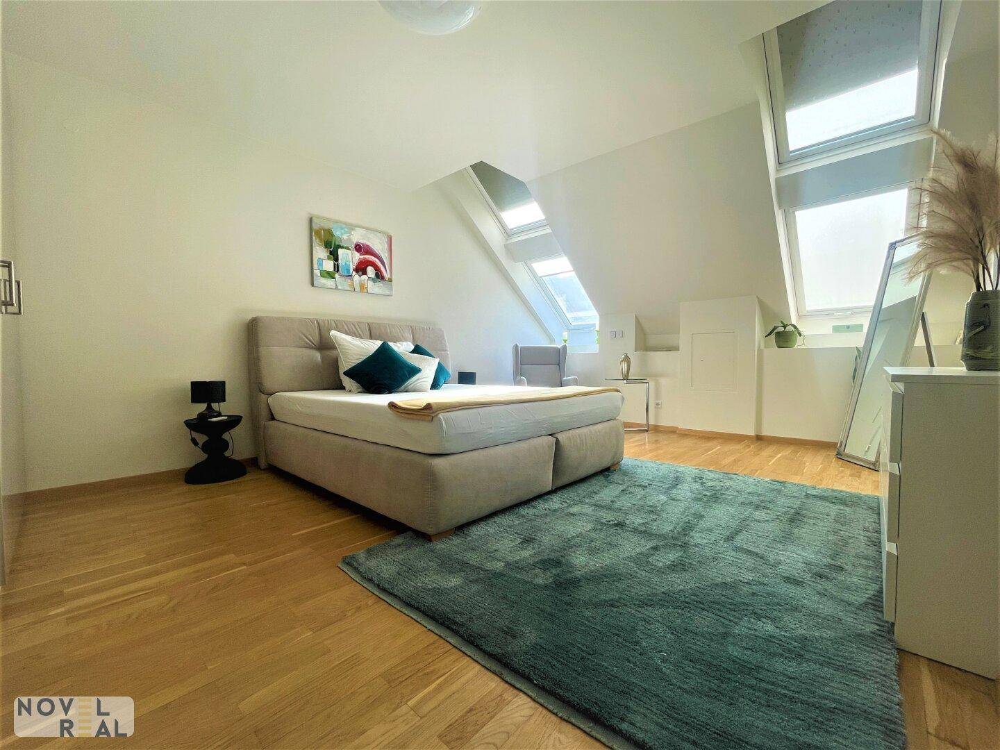 Gemütliches Schlafzimmer im Dachgeschoss mit Holzboden, Teppich und schrägen Wänden mit Dachfenstern.