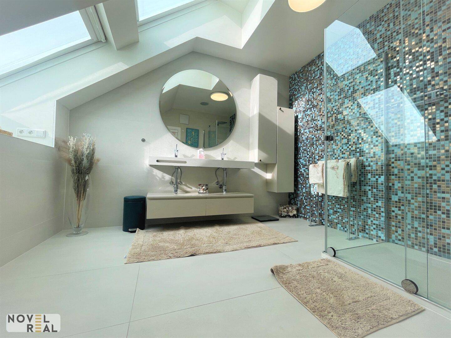Modernes Badezimmer mit Doppelwaschbecken, großer Dusche und farbigen Mosaikfliesen an der Wand.