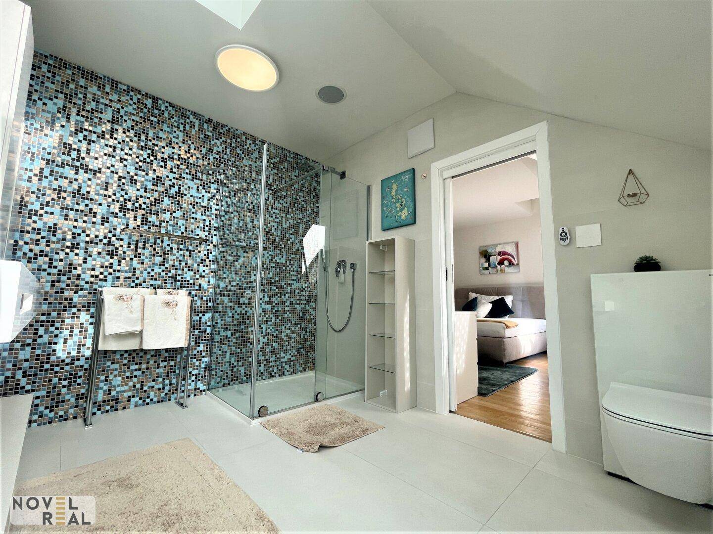 Helles Badezimmer mit Mosaikfliesen, bodengleicher Dusche und direktem Zugang zum Schlafzimmer.