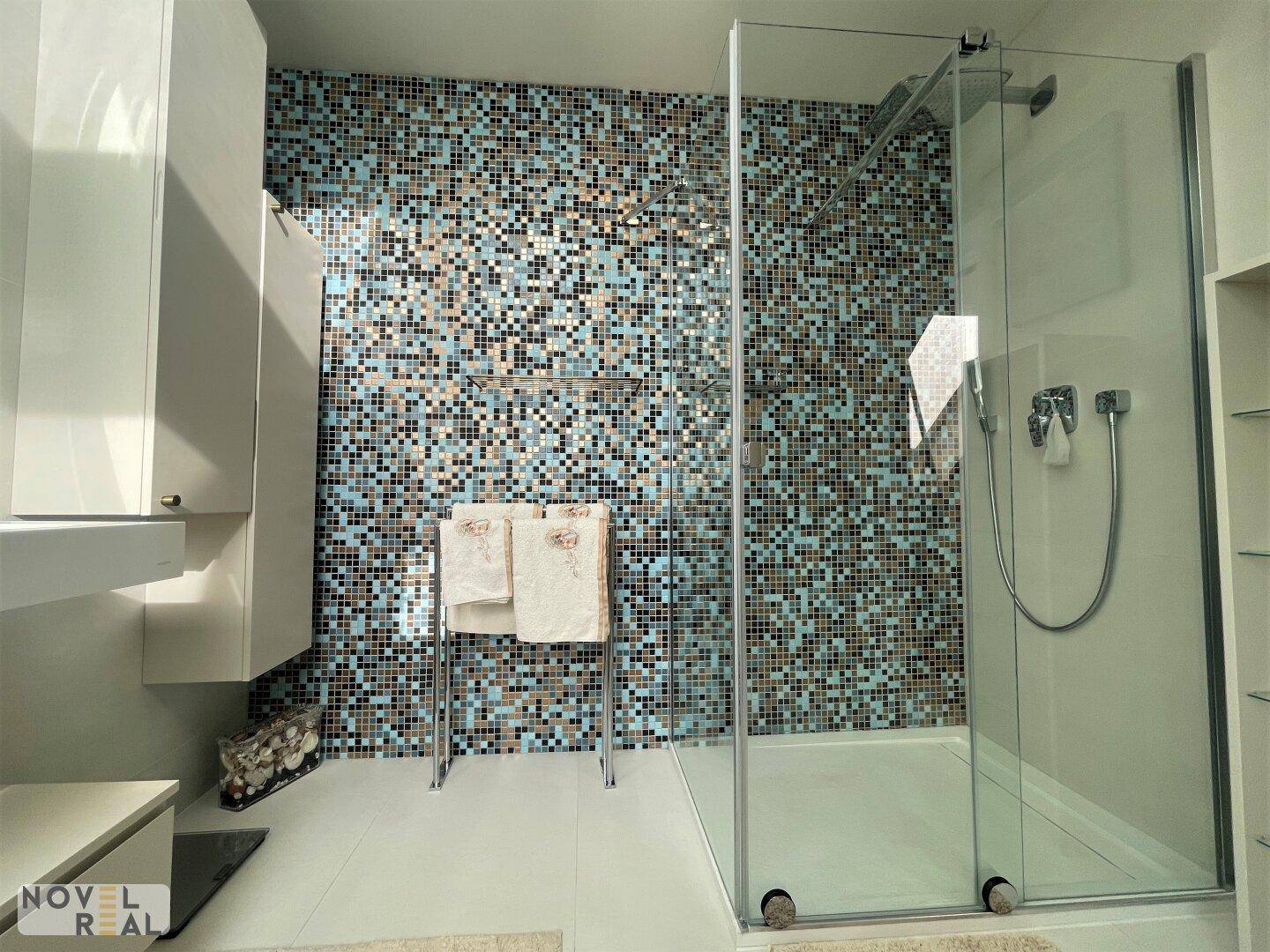 Geräumige, moderne Dusche mit Glaswand, Mosaikfliesen und beheiztem Handtuchhalter.