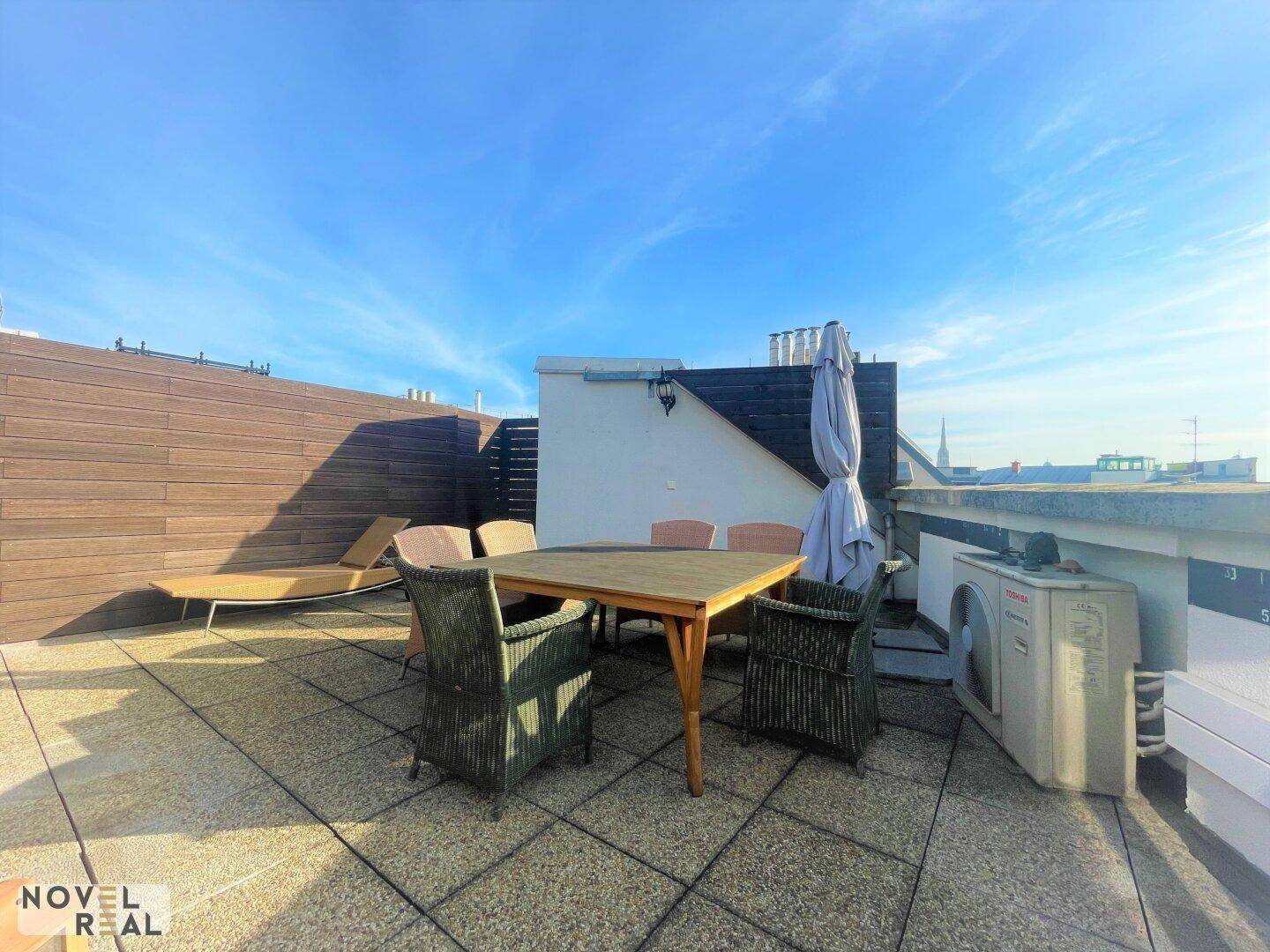 Große Dachterrasse mit Holzboden, Sitzgelegenheiten und weitem Blick über die Stadt.