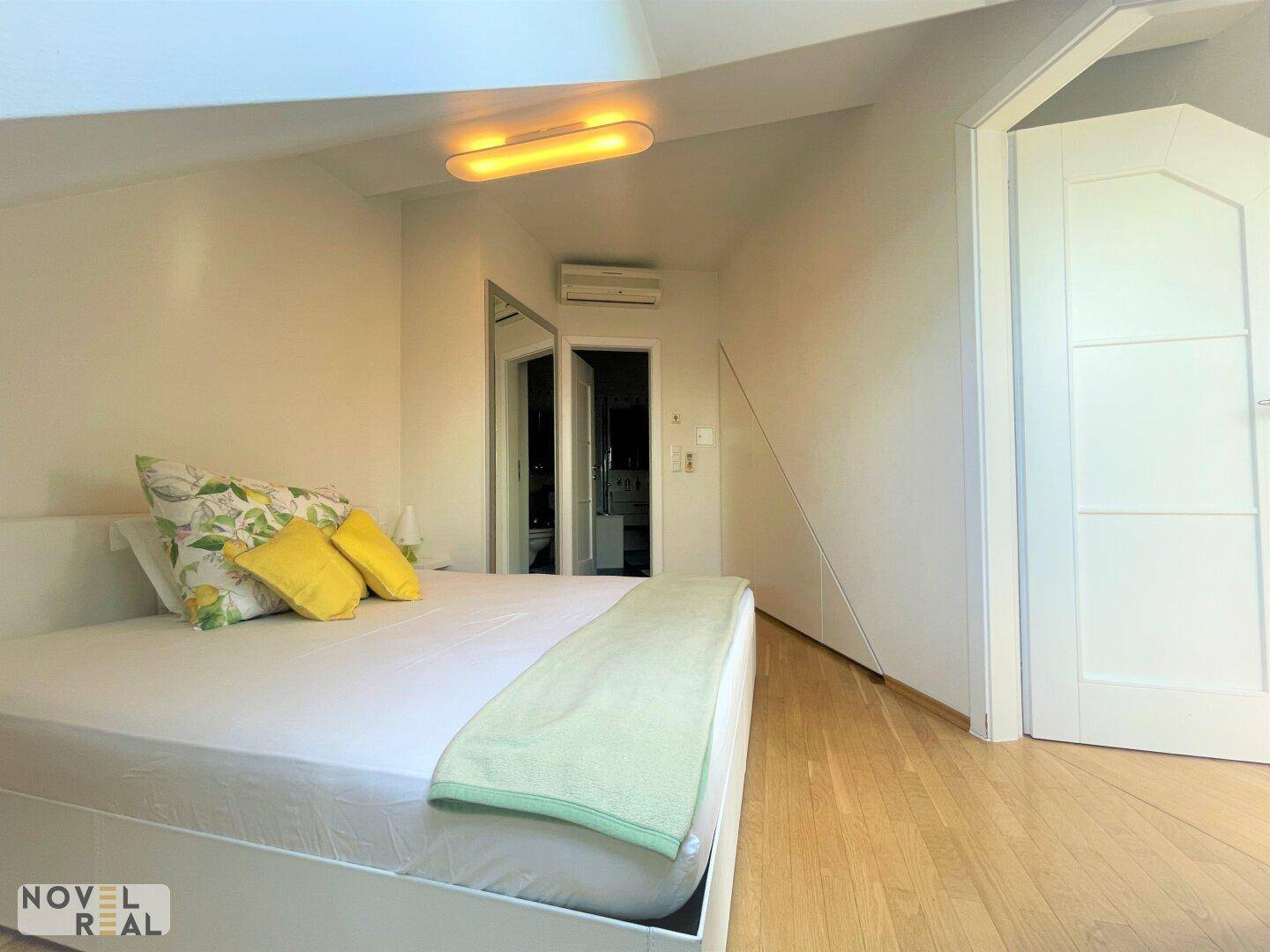 Helles Schlafzimmer mit Holzboden, Klimaanlage und Spiegelschränken im Dachgeschoss.