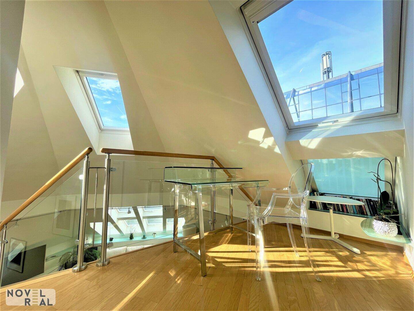 Heller Arbeitsbereich auf der Galerie mit Glasgeländer, Holzboden und Dachfenstern.