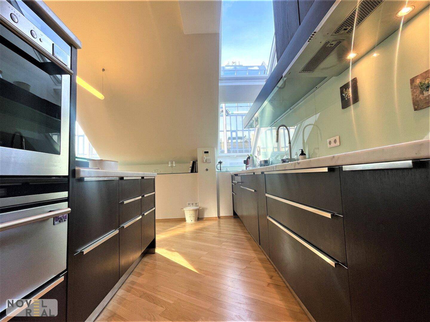Moderne Küche mit dunklen Schränken, integriertem Backofen und viel Tageslicht.