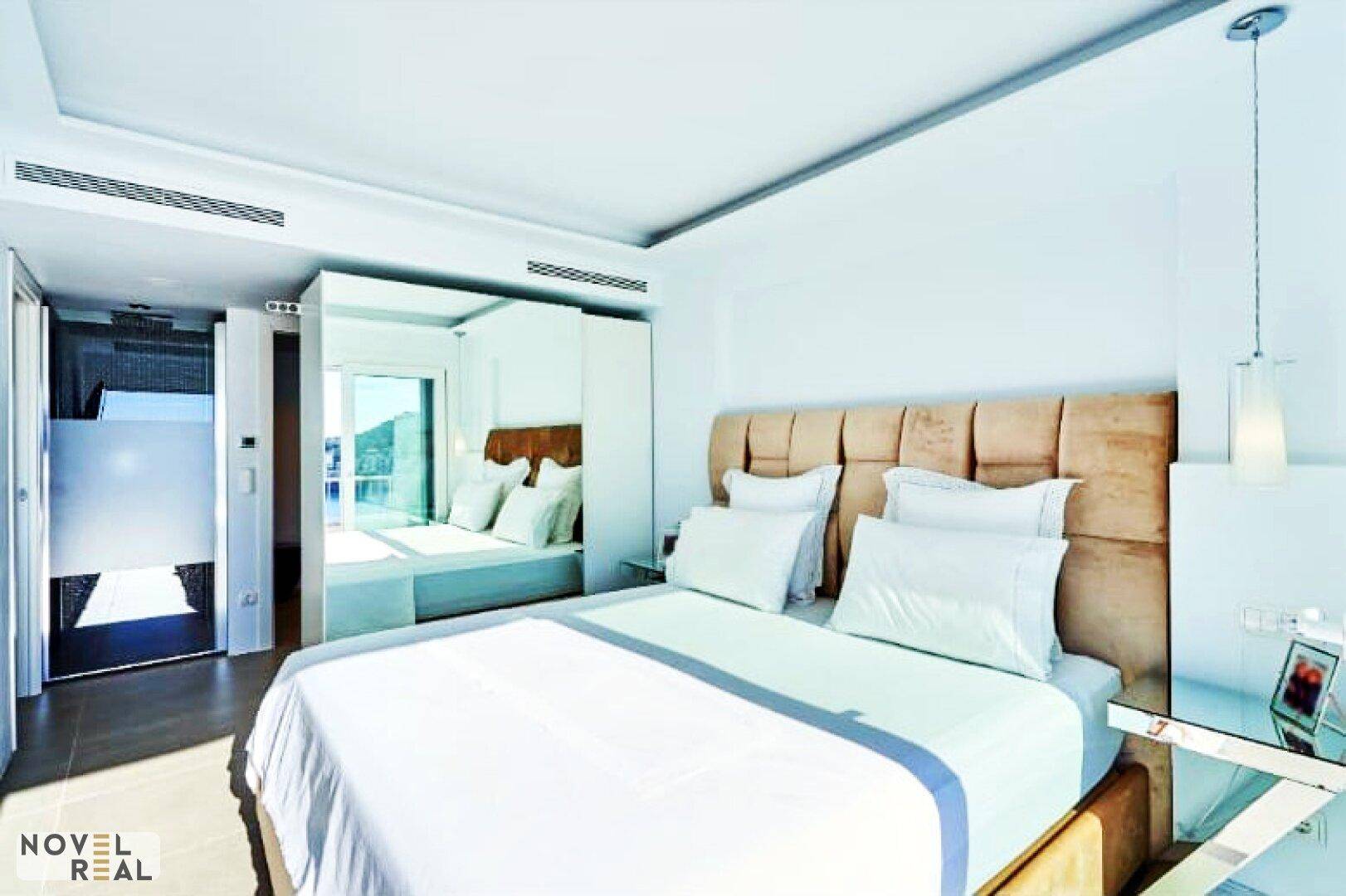 Helles Schlafzimmer mit modernem Bett, Spiegelschränken und Zugang zu einem weiteren Raum.