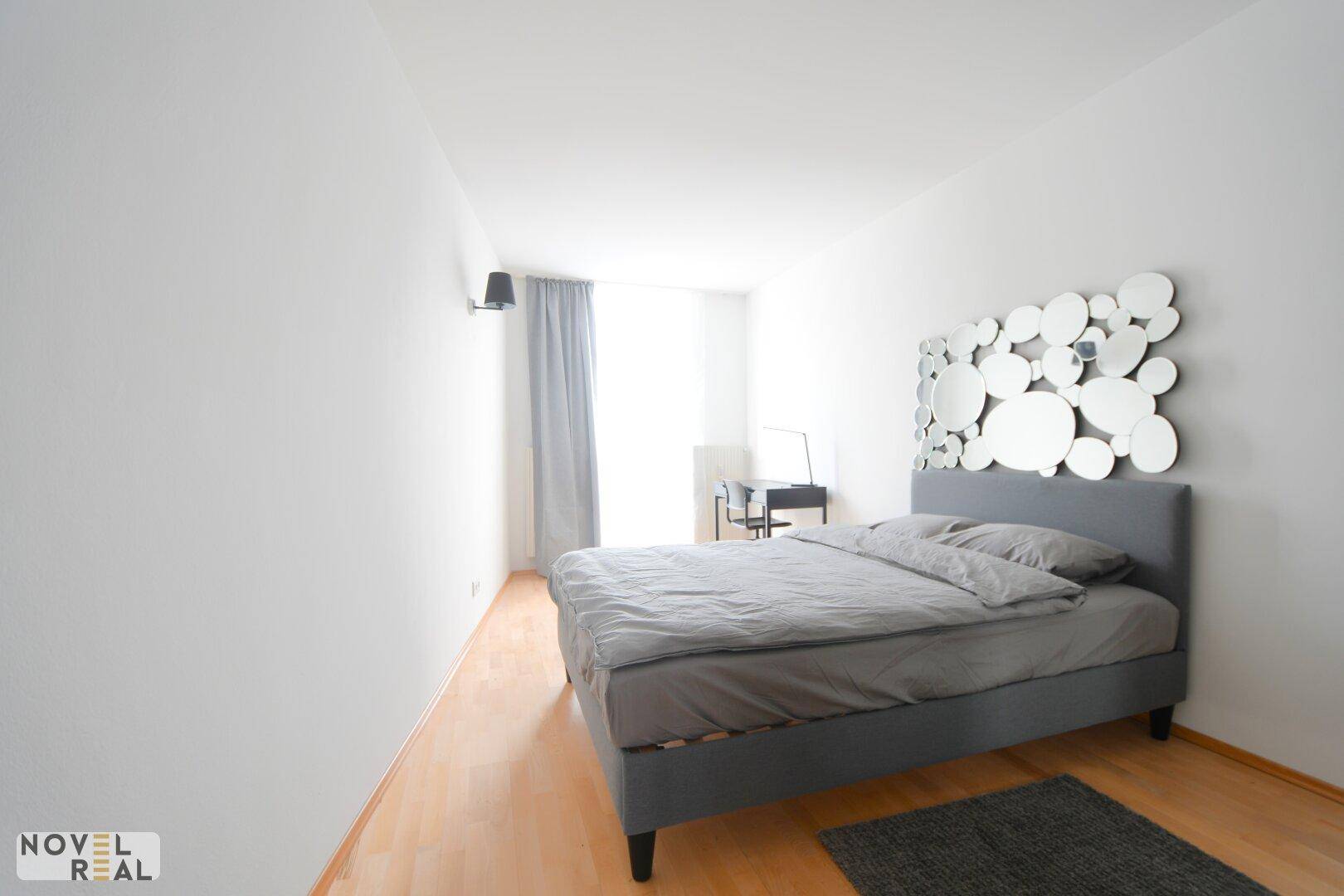 Geräumiges Schlafzimmer mit modernem Bett, Spiegeldekoration und hellem Holzfußboden.