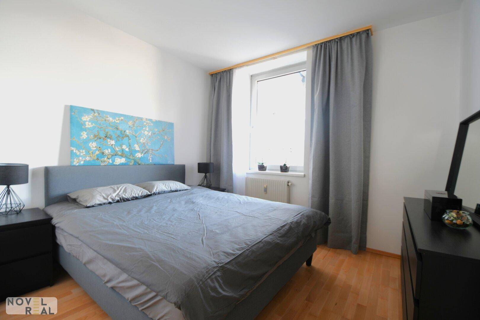 Helles Schlafzimmer mit großem Fenster, Vorhängen und einem bequemen Doppelbett.