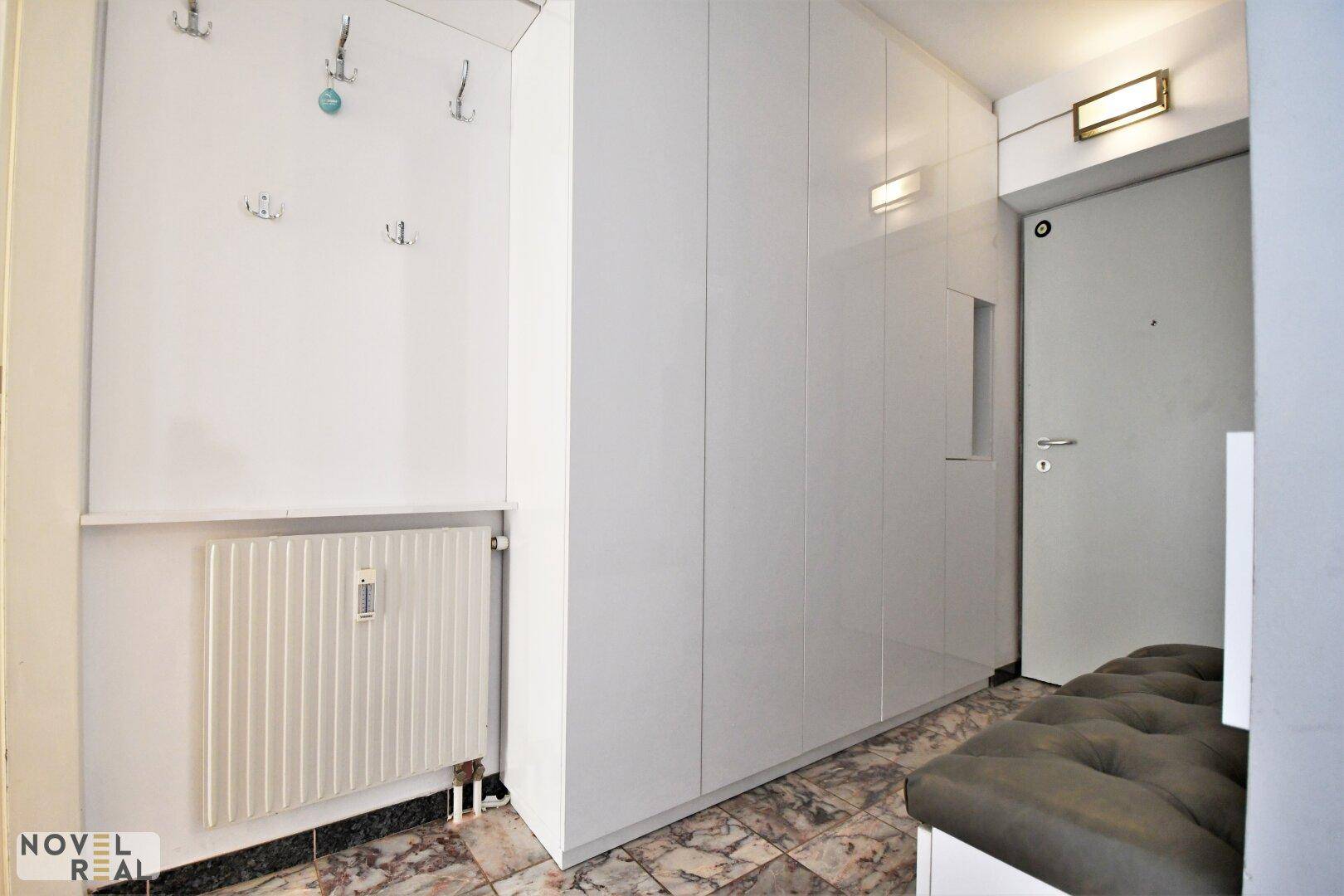 Heller Flur mit glänzenden Einbauschränken, Heizkörper und Garderobenhaken.