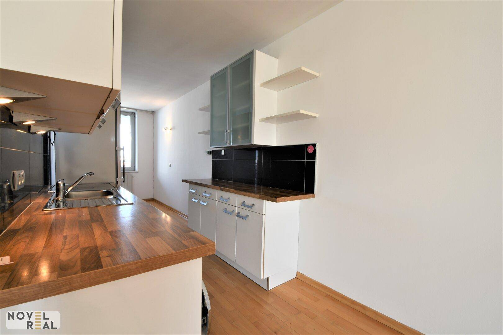 Moderne Küche mit weißen Oberschränken, Holztheke und schwarzem Fliesenspiegel.
