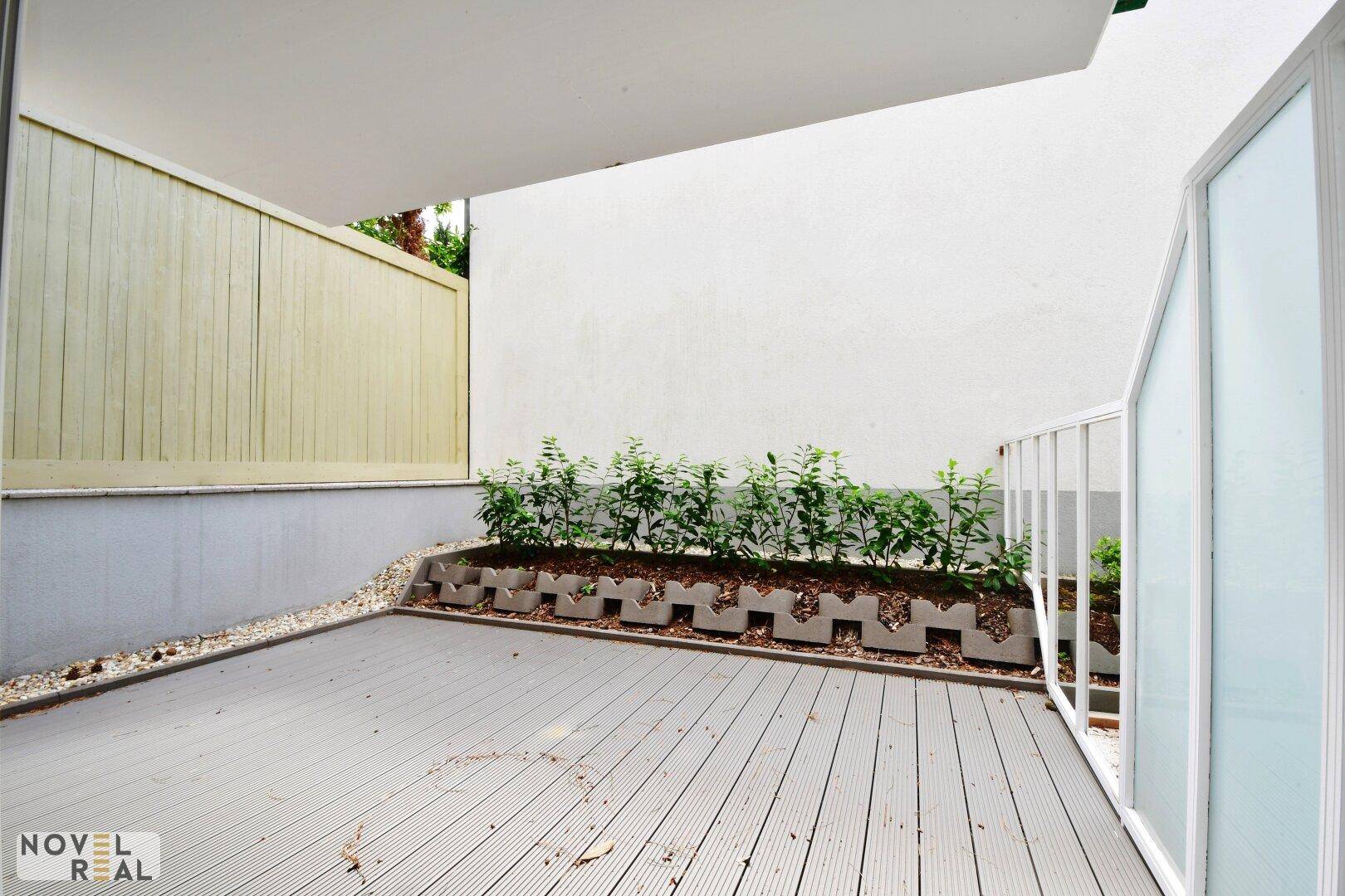 Geräumige Terrasse mit Holzboden, Pflanzenbeeten und einer schützenden Wand.