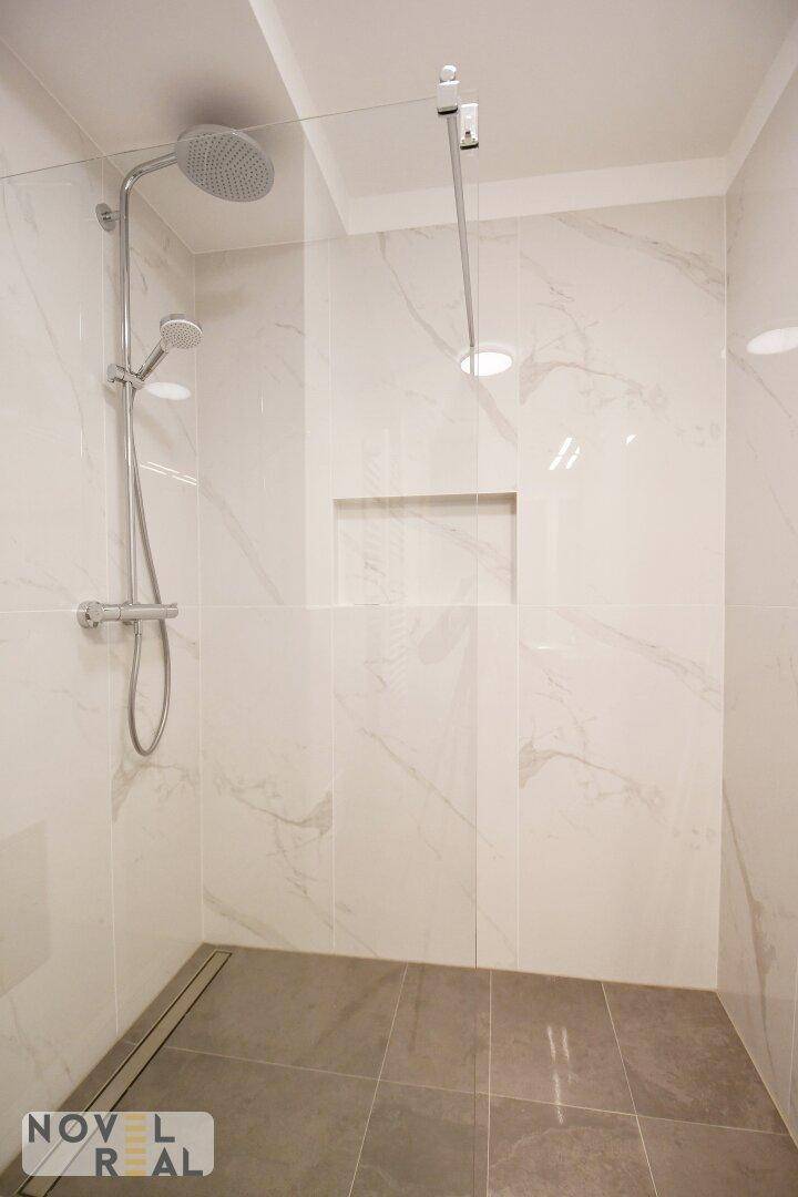 Geräumige, begehbare Dusche mit modernen Fliesen und Regenduschkopf.