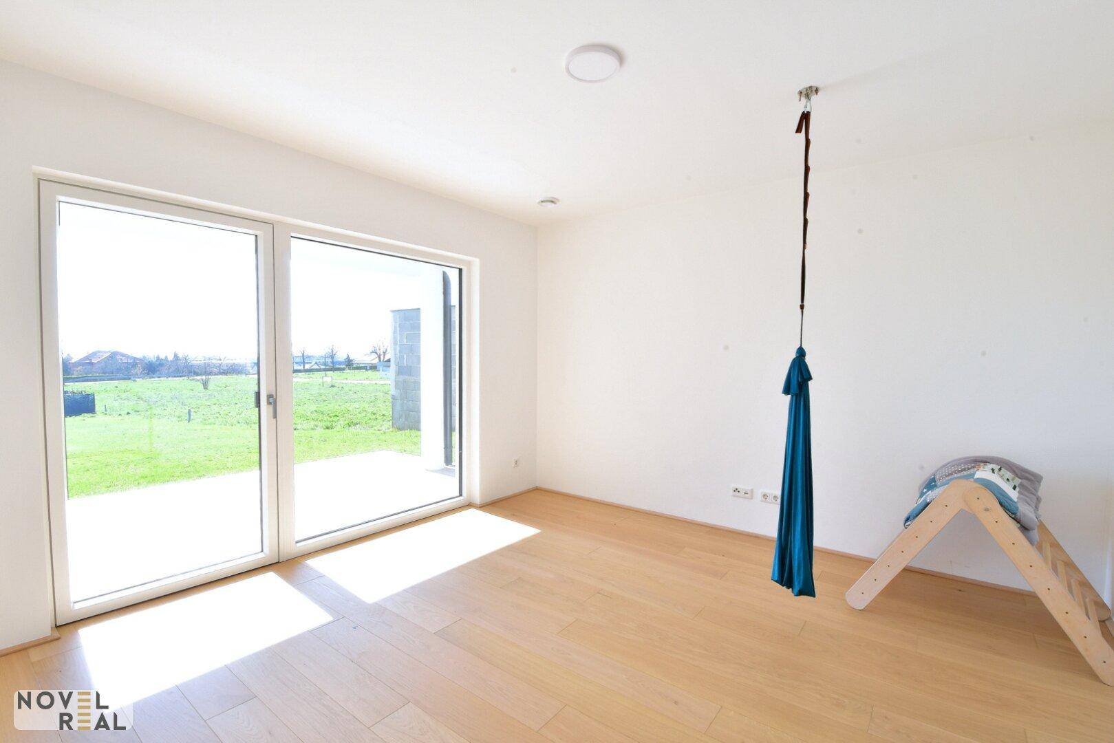 Helles Zimmer mit Holzboden, großen Schiebetüren und Blick ins Grüne.