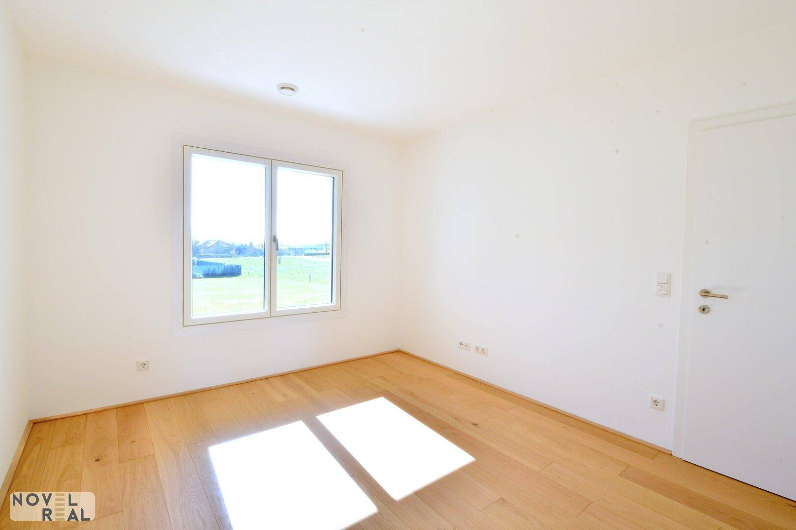 Helles Zimmer mit Holzboden und einem großen Fenster, das viel Tageslicht hereinlässt.