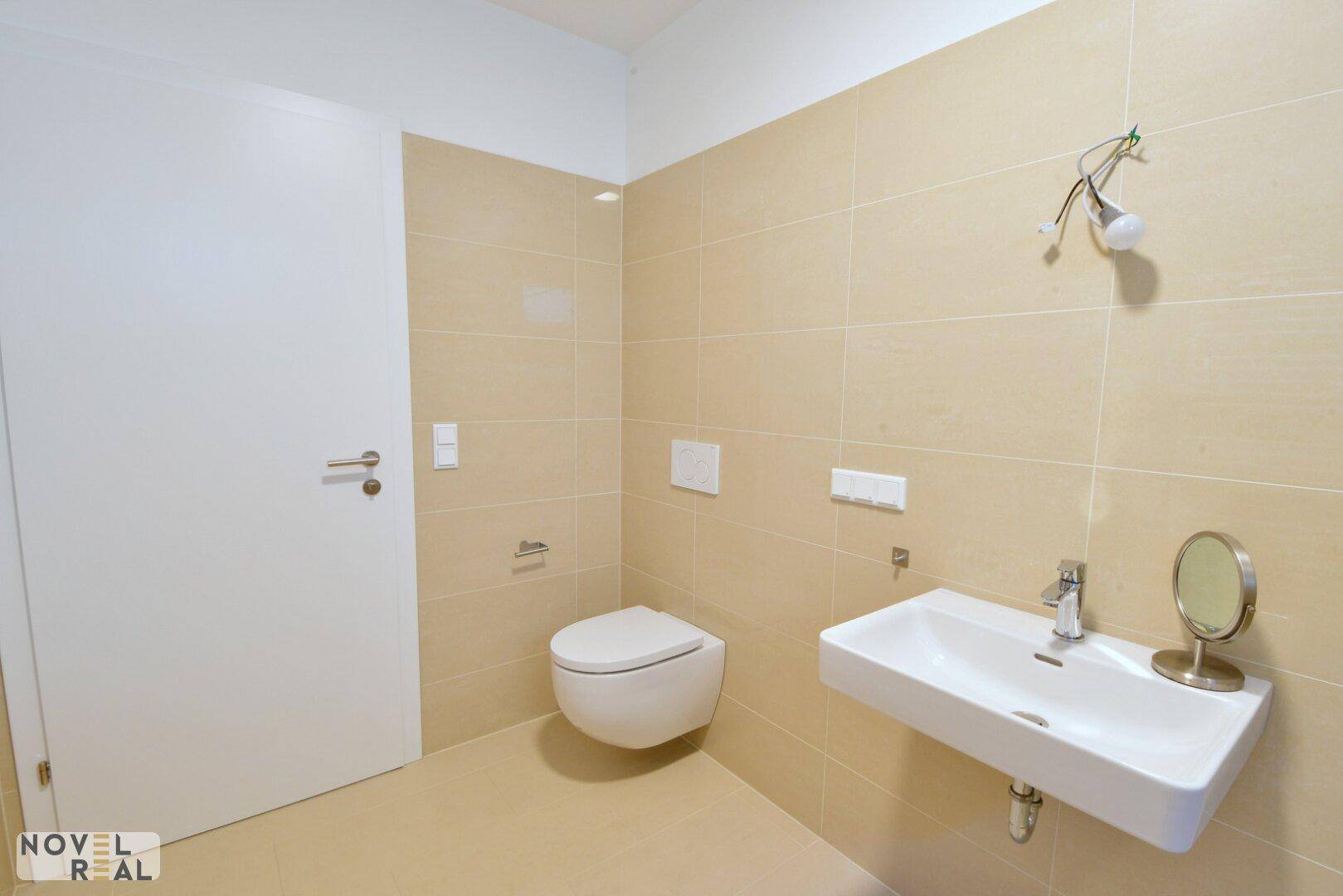 Modernes Badezimmer mit wandhängendem WC, Waschbecken und beigen Fliesen.