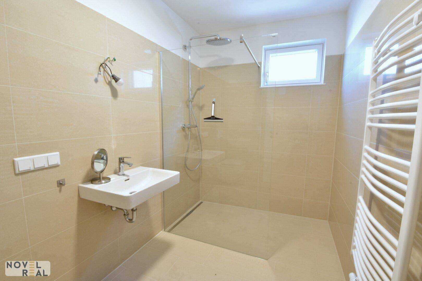 Modernes Badezimmer mit begehbarer Dusche, beigen Fliesen und beheiztem Handtuchhalter.
