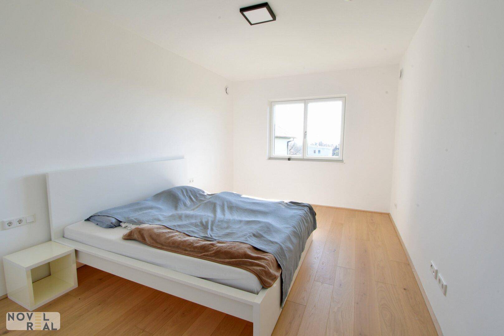 Helles Schlafzimmer mit Doppelbett, Holzboden und einem Fenster.