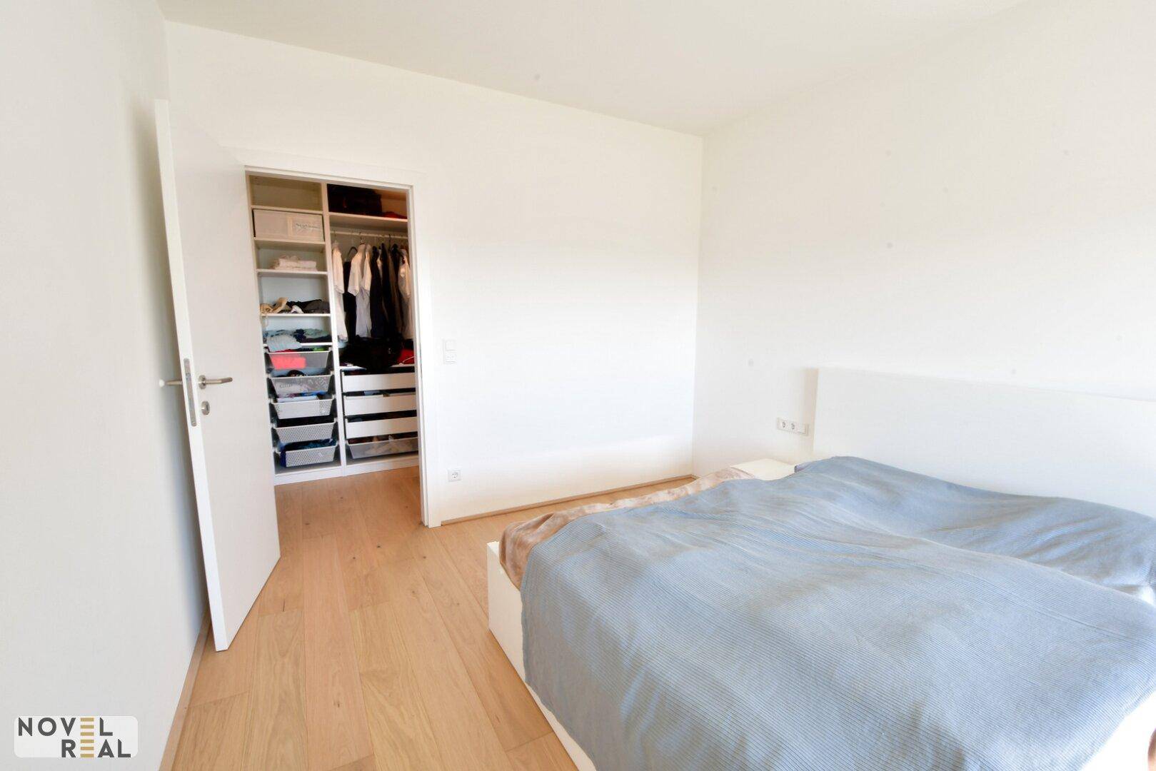 Schlafzimmer mit Holzboden und offenem Zugang zu einem begehbaren Kleiderschrank.
