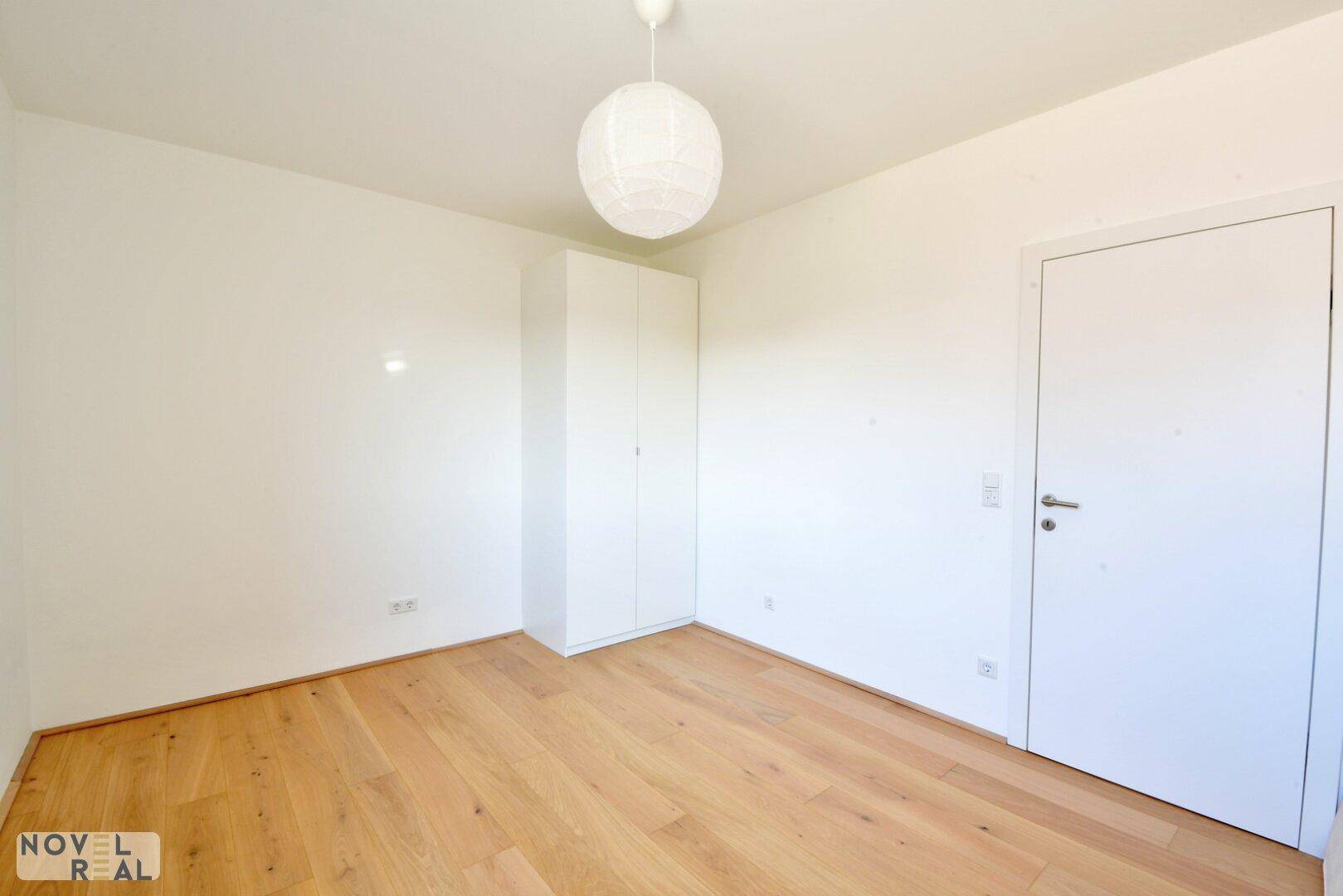 Geräumiges Kinderzimmer mit weißem Kleiderschrank, Holzboden und viel Tageslicht.