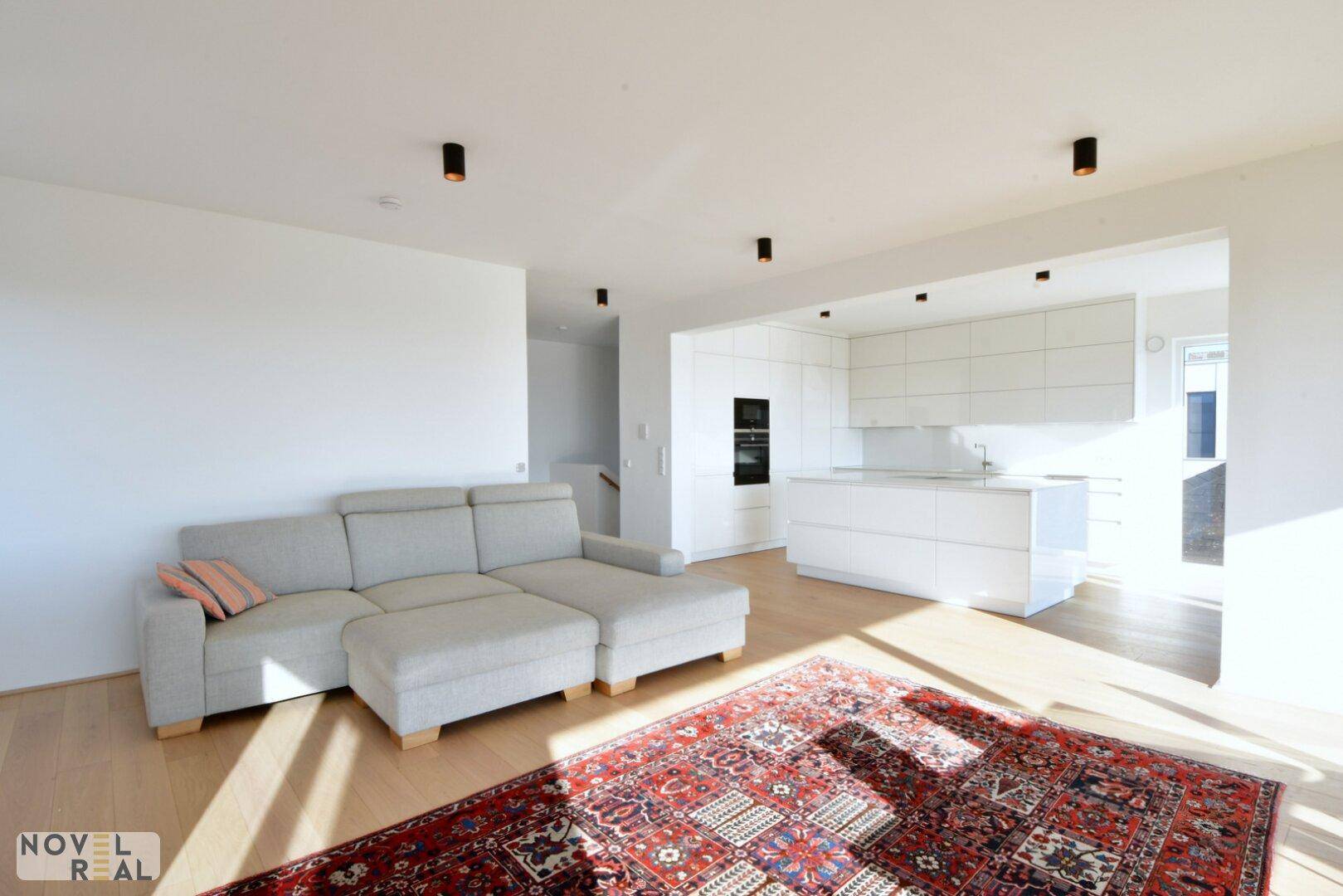 Offener Wohnbereich mit beigem Sofa, Holzboden und Blick auf die moderne Küche.