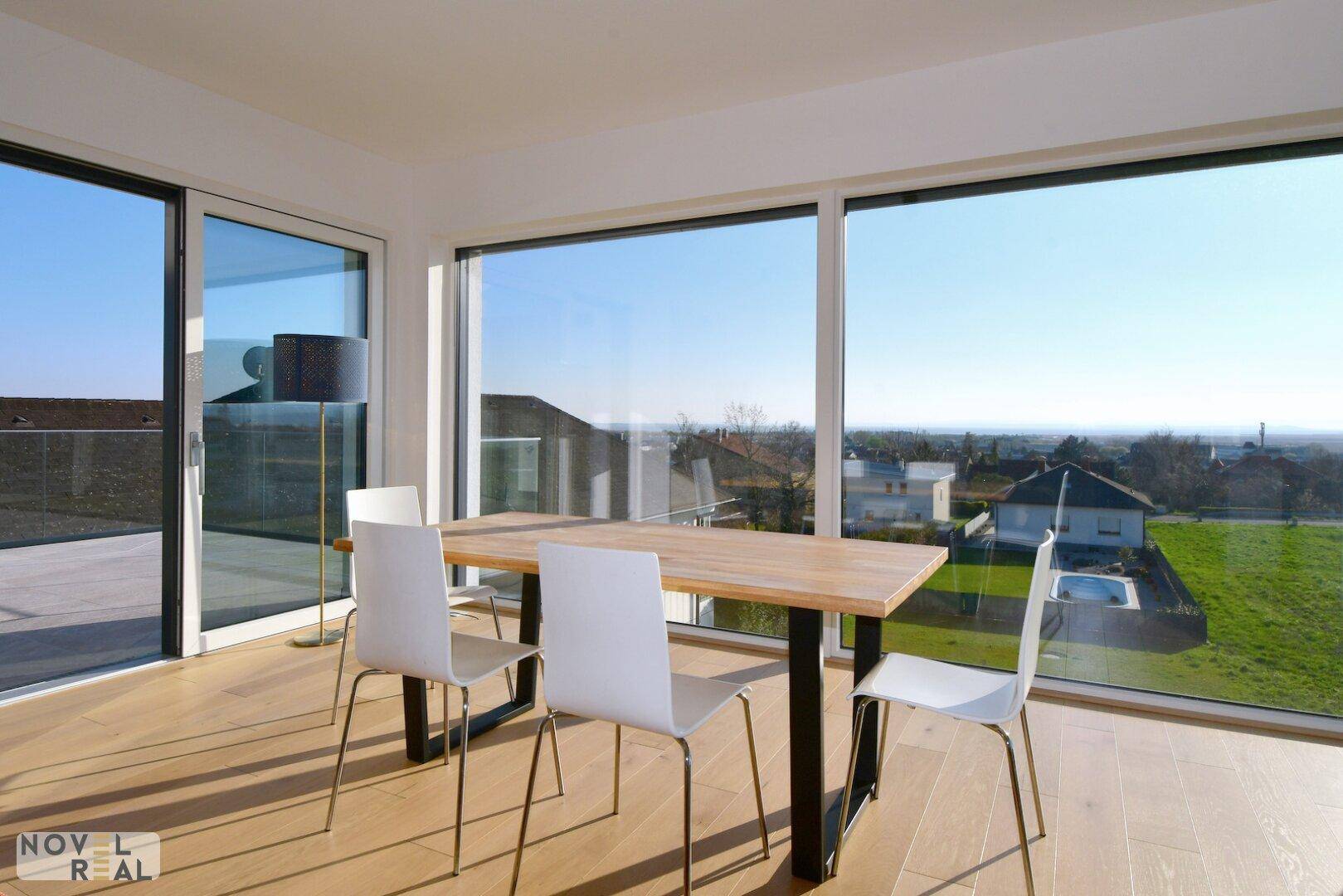 Lichtdurchfluteter Essbereich mit Holztisch, weißen Stühlen und Panoramablick durch große Fenster.