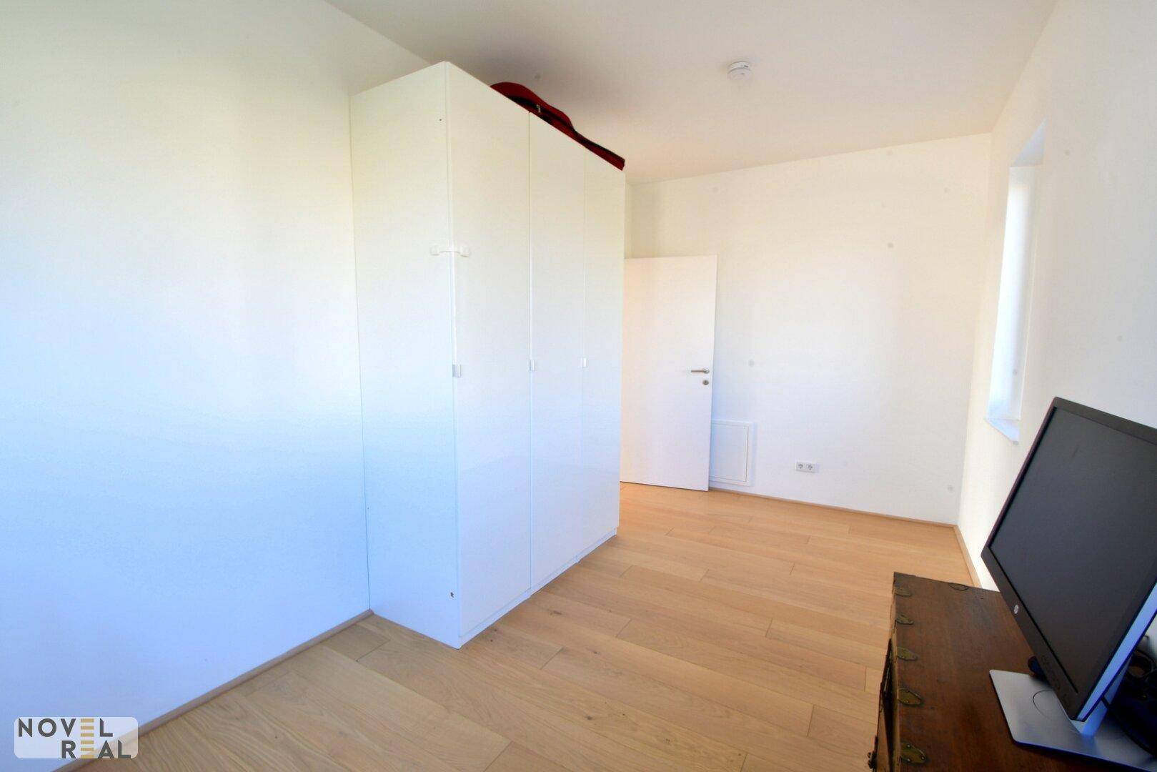 Helles Schlafzimmer oder Arbeitszimmer mit weißem Kleiderschrank und Holzboden.
