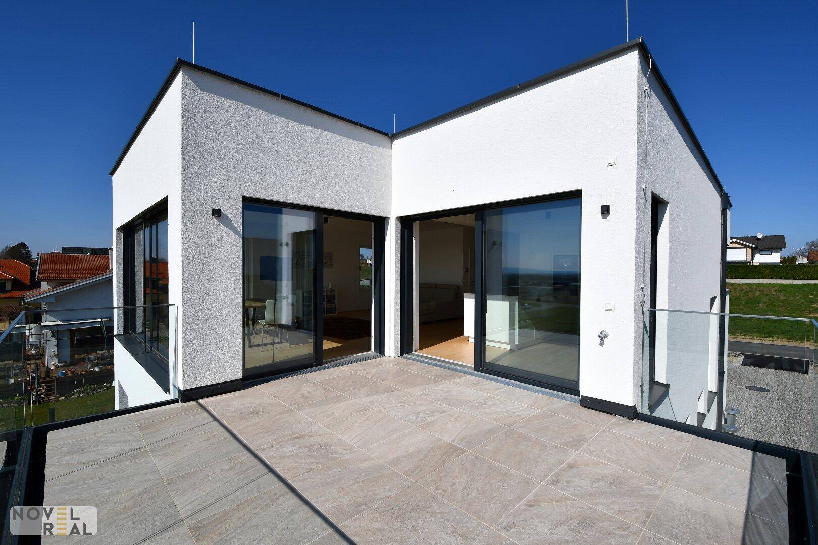 Moderne Architektur mit weißer Fassade, großen Glasfronten und einer weitläufigen Dachterrasse.