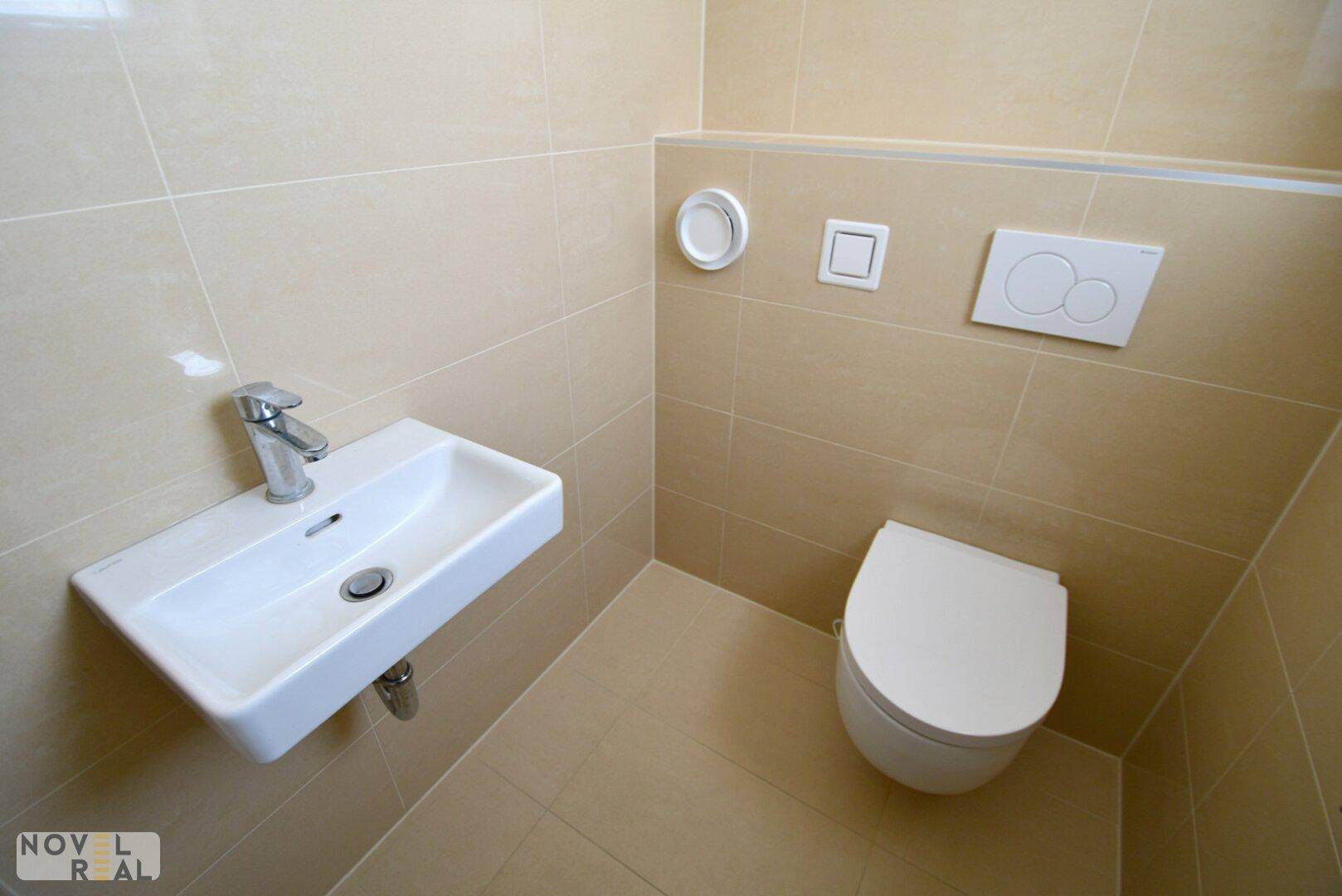 Modernes Gäste-WC mit beigen Fliesen, wandhängendem WC und kleinem Waschbecken.