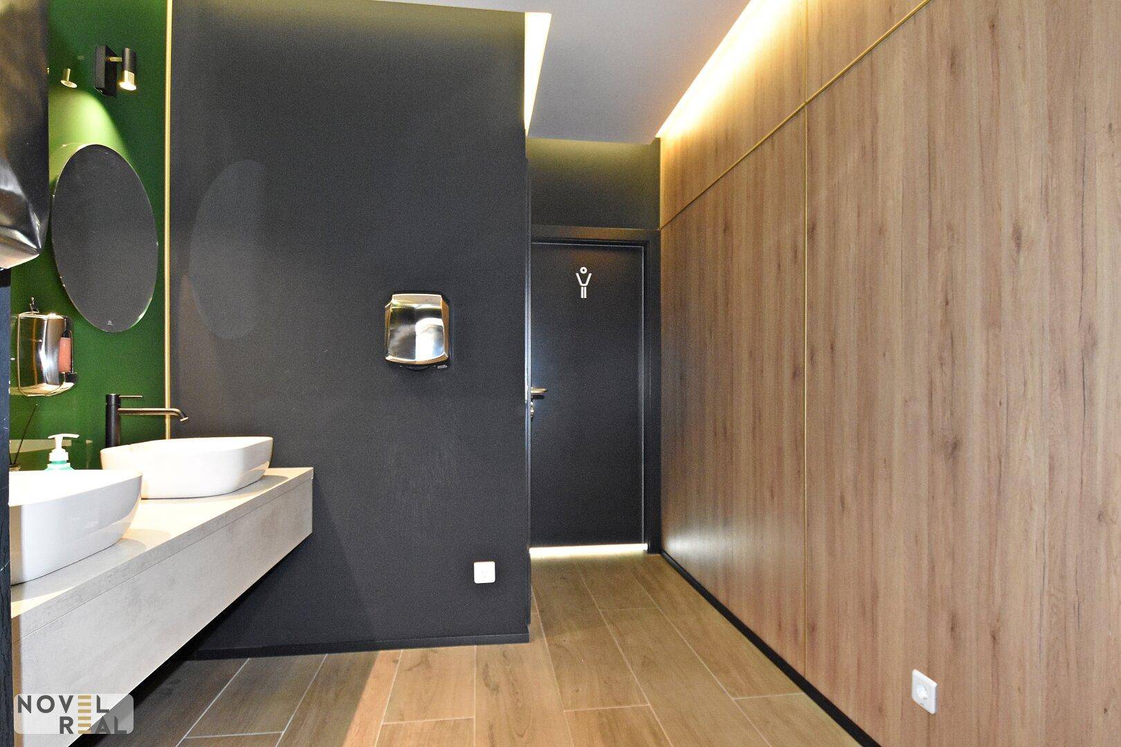 Modernes Badezimmer mit zwei Waschbecken, dunklen Wänden und Holzverkleidung, ausgestattet mit einem Händetrockner.