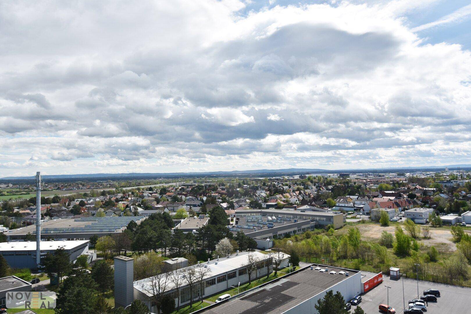 Breiter Überblick über eine Stadtlandschaft mit Industriegebäuden, Wohngebieten und viel Grün.
