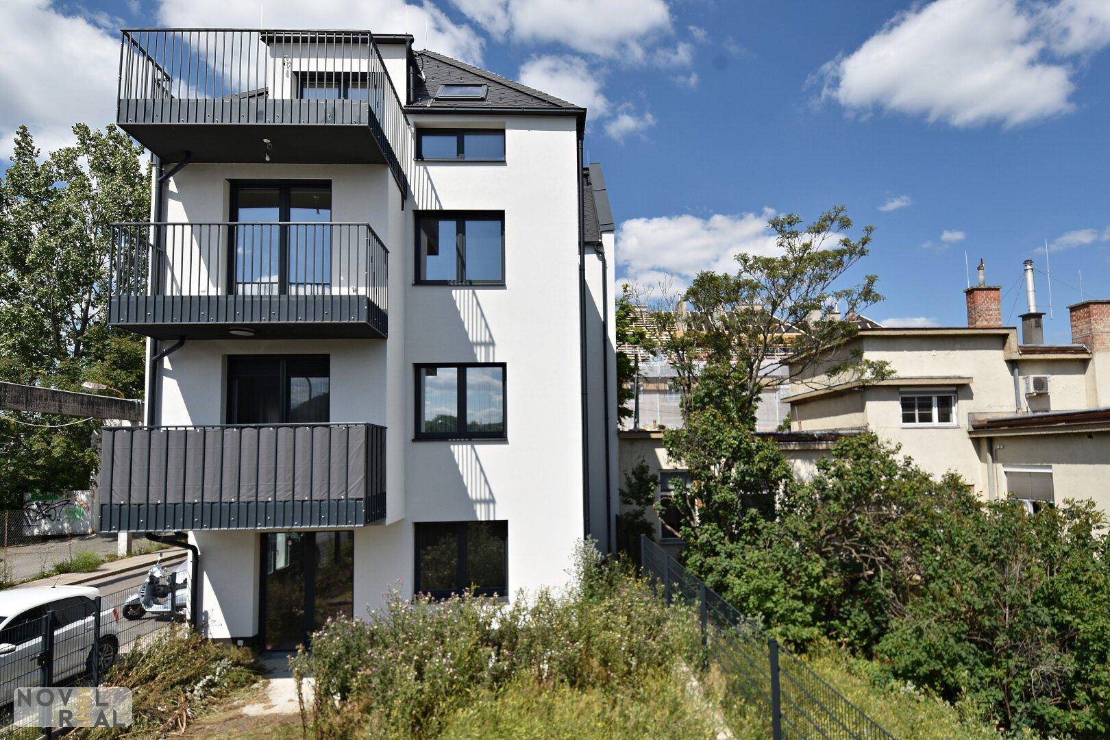 Moderne Wohnhausfassade mit mehreren Balkonen und großen Fenstern unter blauem Himmel.