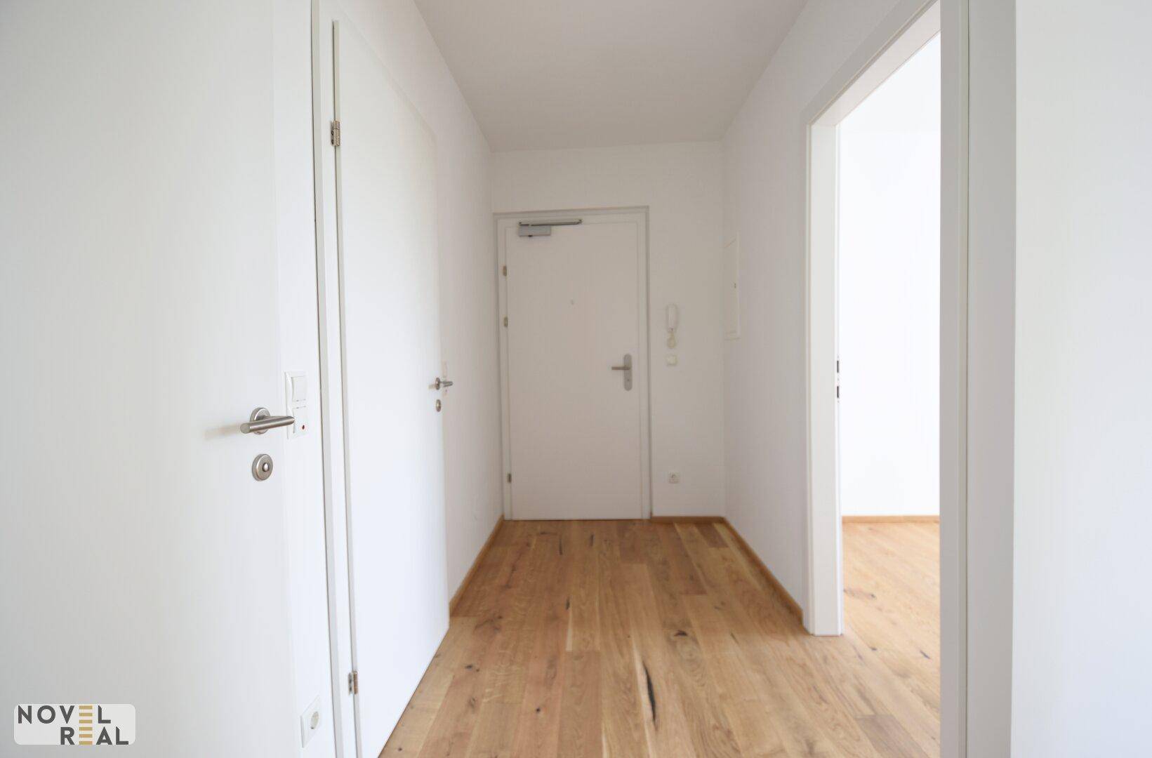 Heller Eingangsbereich mit Holzboden und mehreren Türen, die zu den verschiedenen Räumen führen.