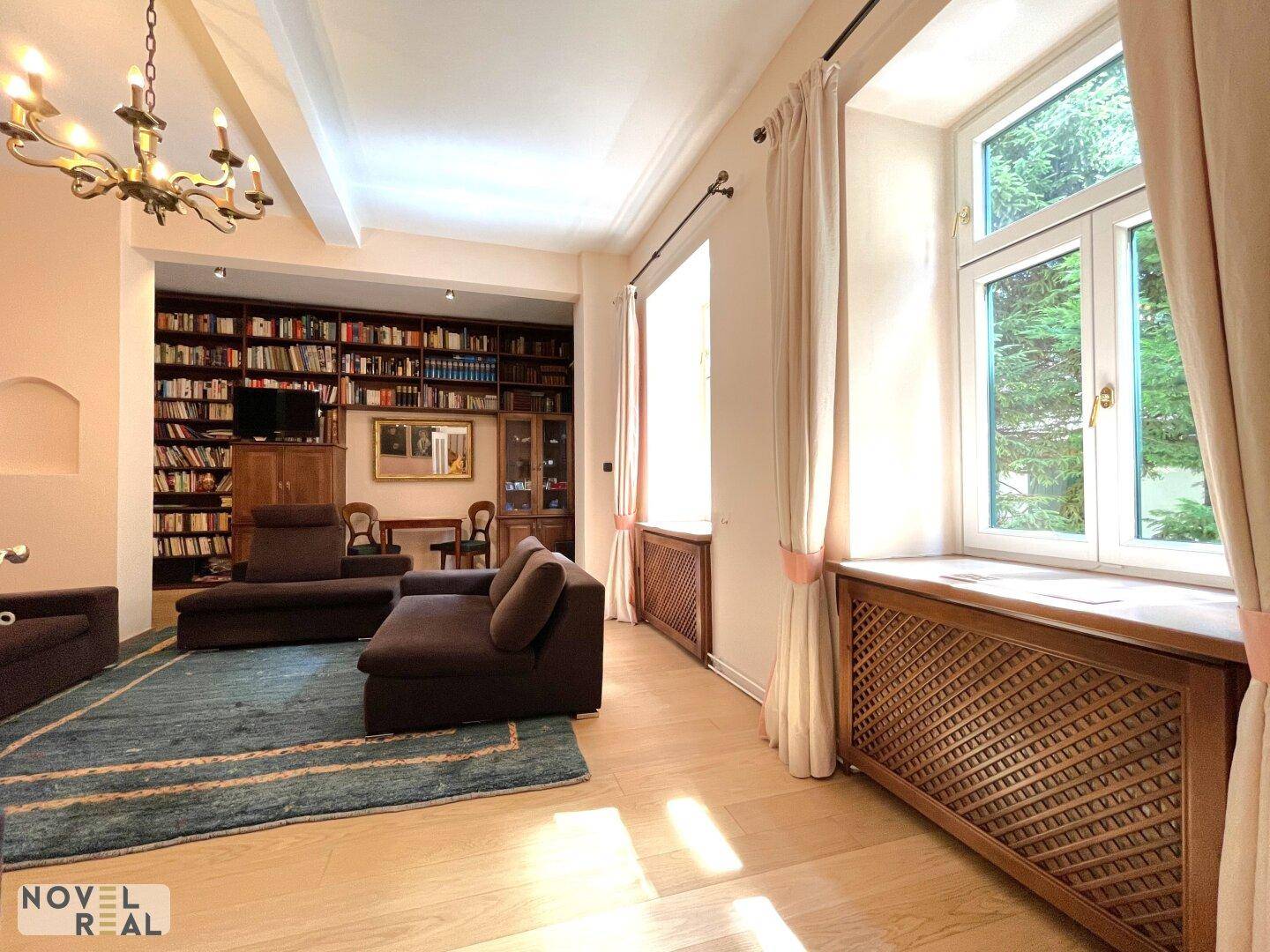 Gemütliches Wohnzimmer mit großer Bücherwand, Parkettboden und viel Tageslicht.